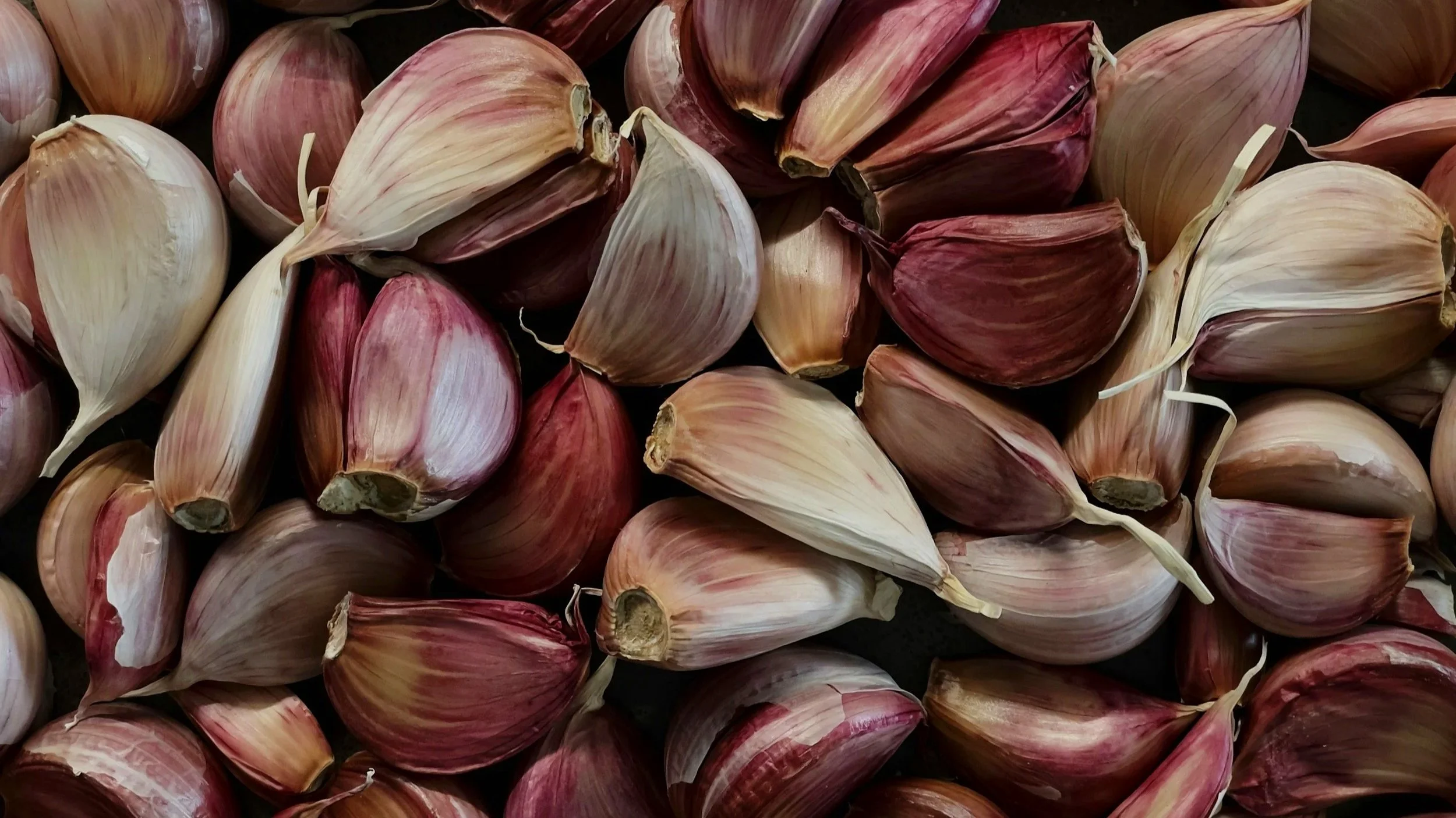 Close-up of multiple garlic bulbs with papery skins in shades of white, pink, and purple.