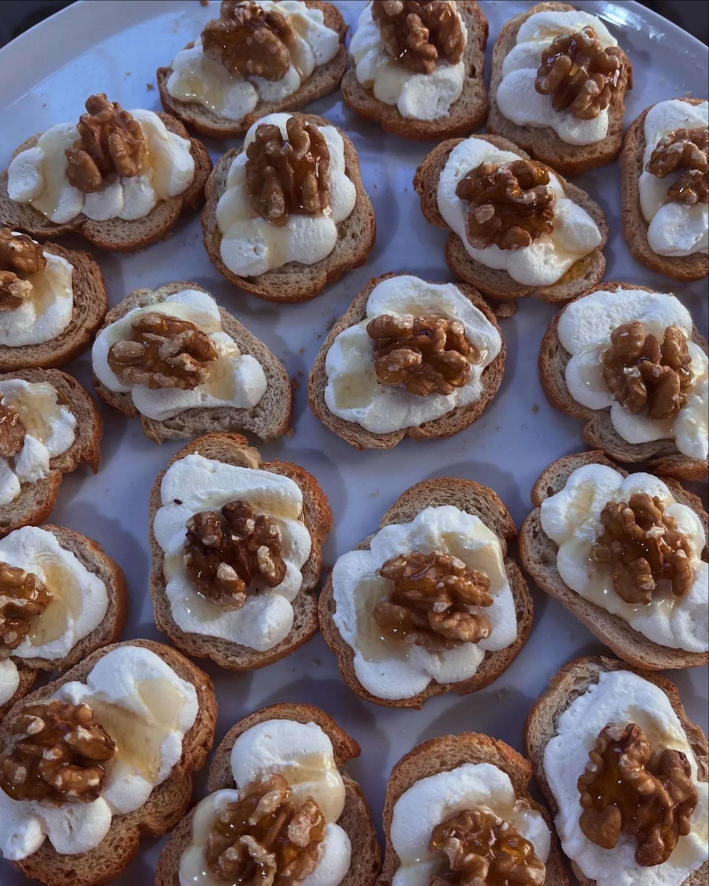 Open-faced bread slices topped with cream cheese, walnuts, and honey, arranged on a white platter.