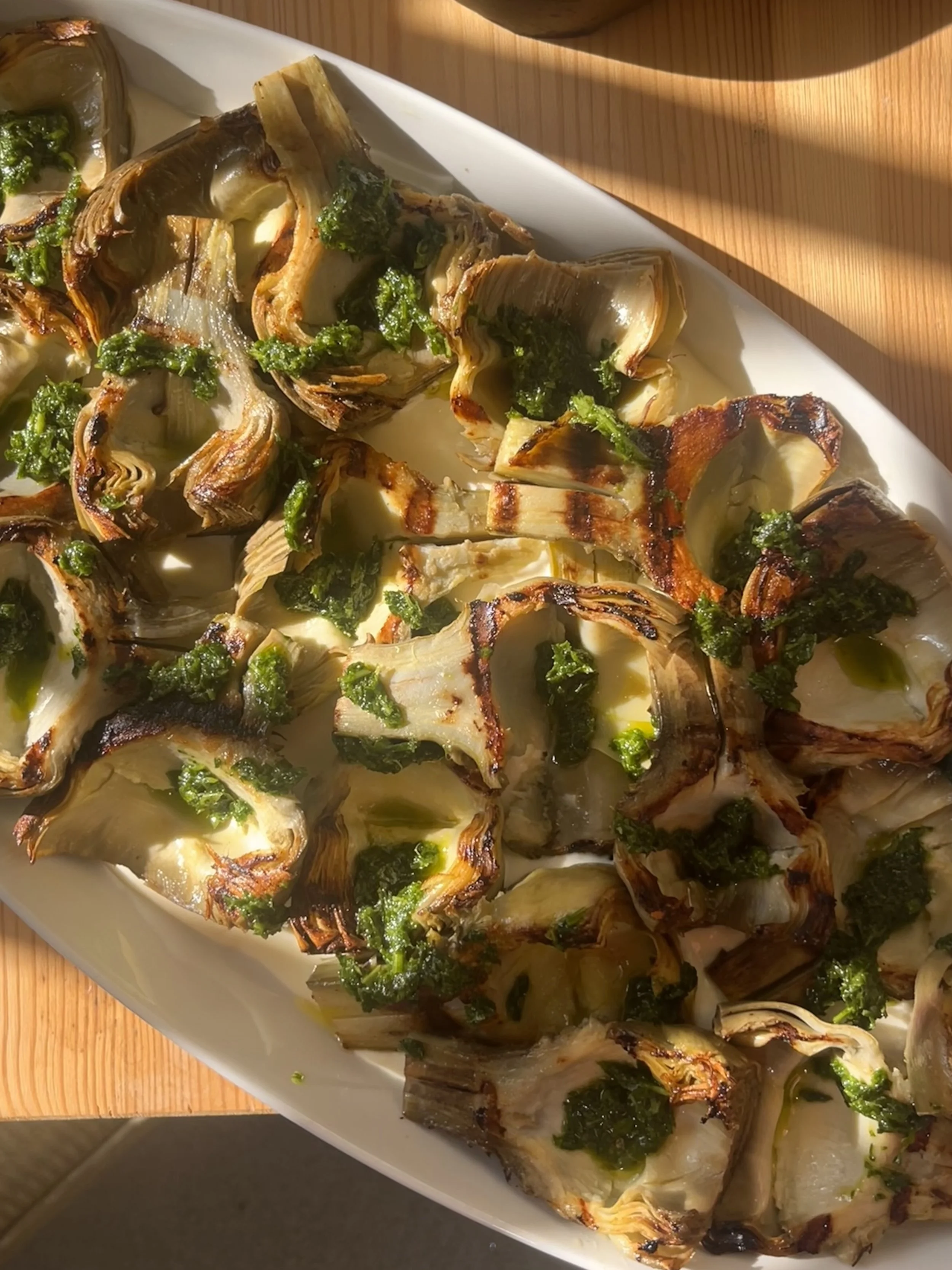 Grilled artichoke halves garnished with chopped herbs on a white platter.