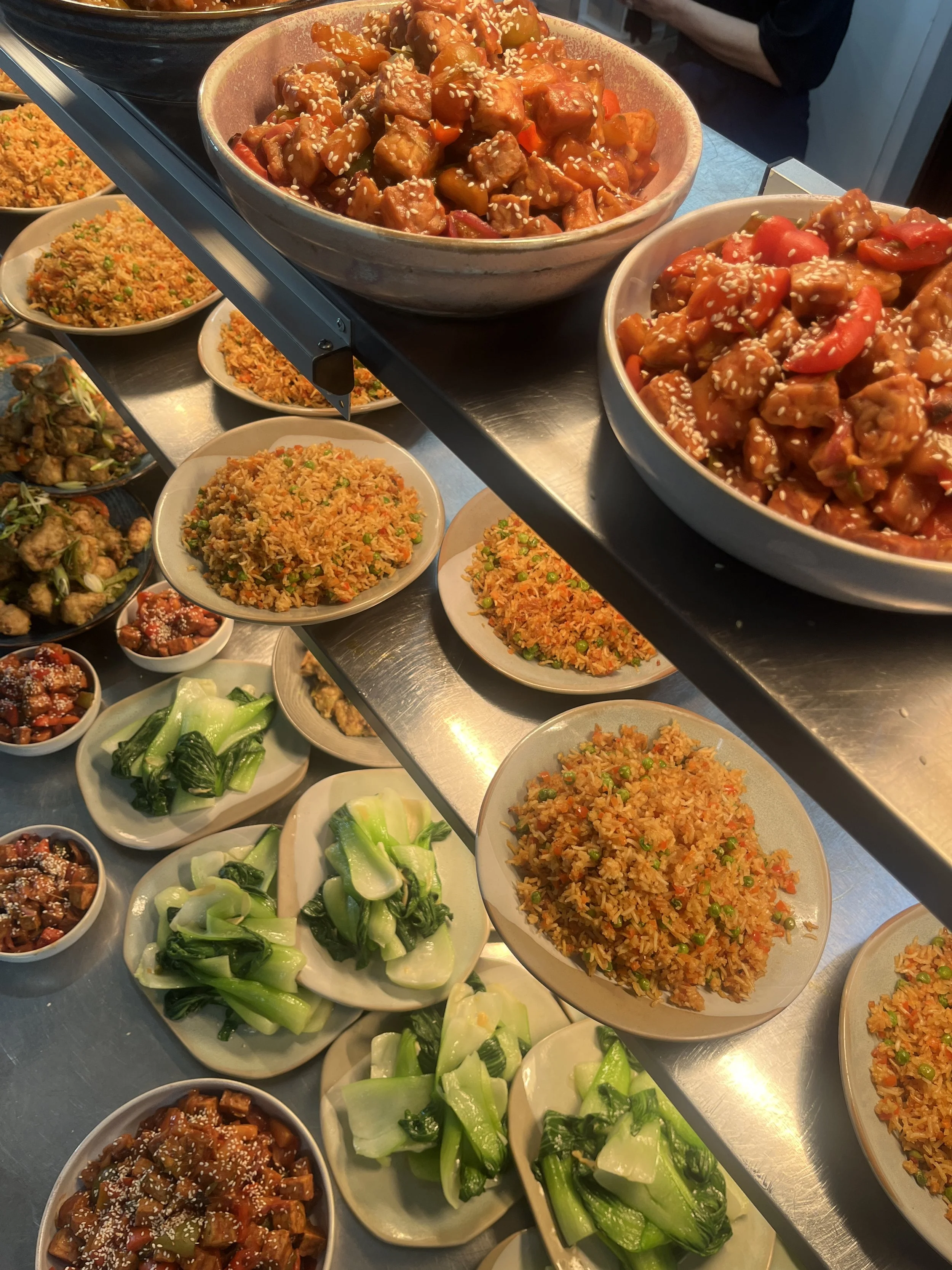 Assorted Asian dishes including fried rice, stir-fried vegetables, and meat in sauce with sesame seeds, arranged on a buffet table.