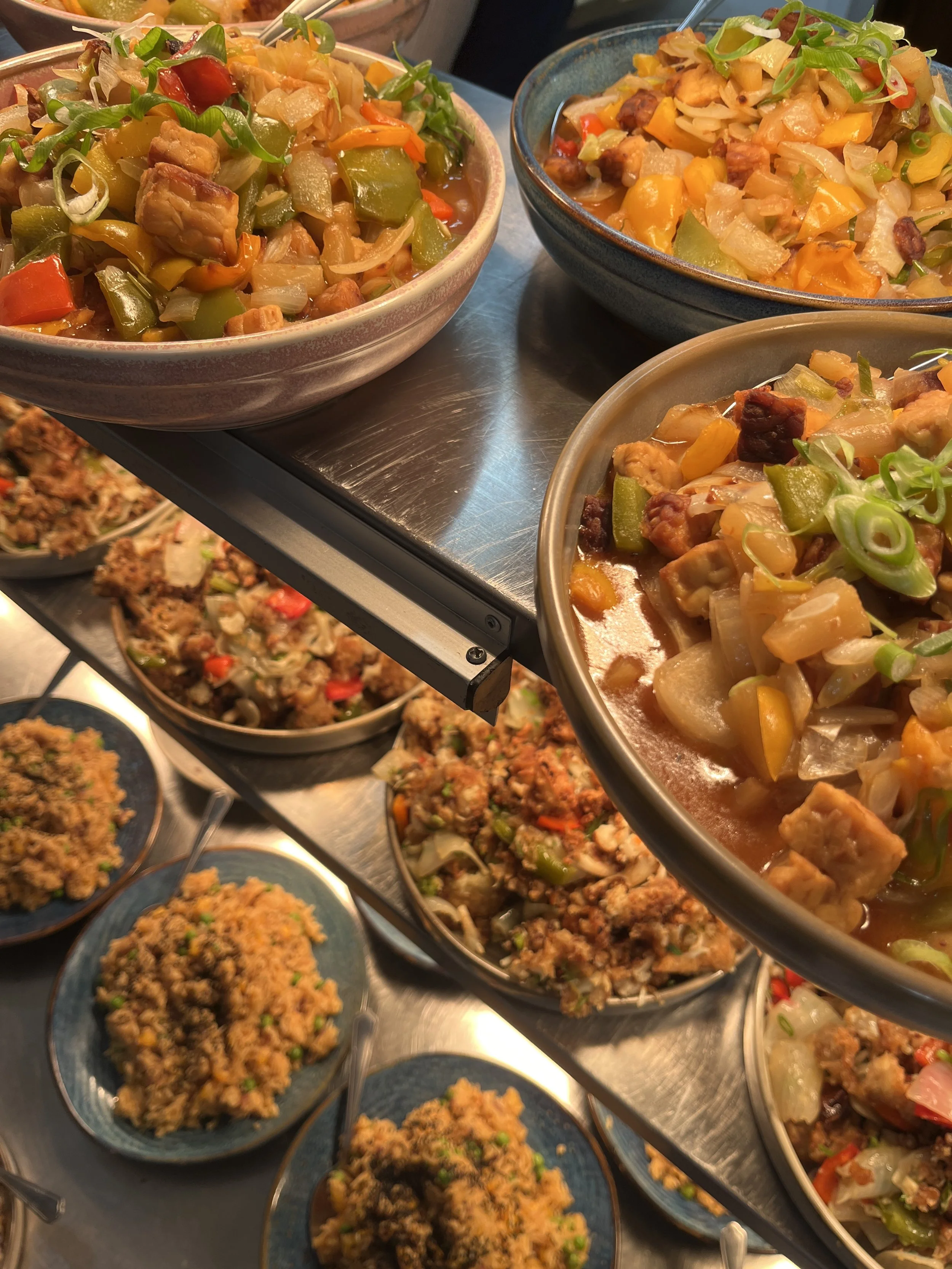 A display of various colorful Asian-style stir-fried vegetables and dishes in bowls at a buffet or restaurant setting.