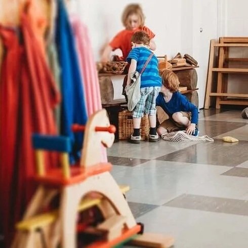 Group of children in their classroom, playing together with a wooden rocking horse in the foreground.