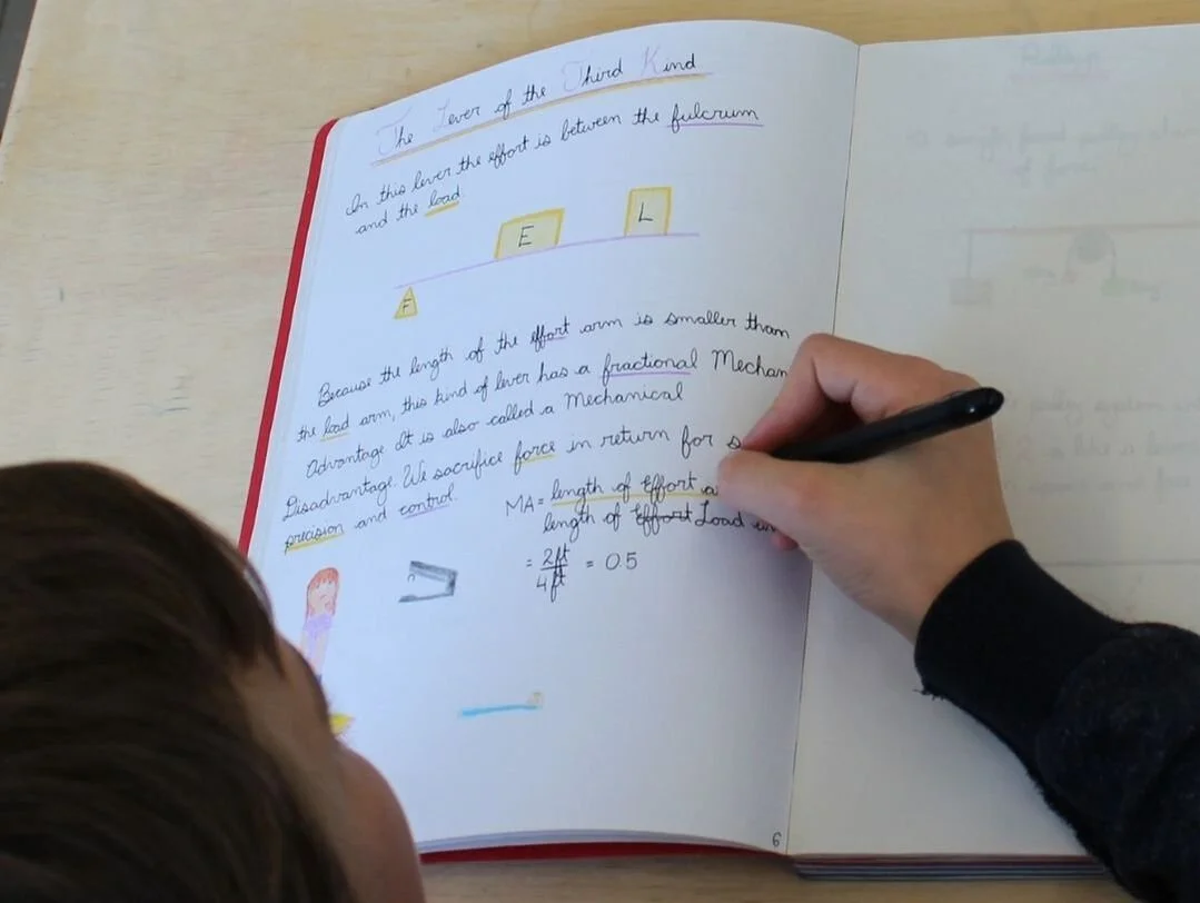 A school-aged child is writing in a notebook with notes and highlighted sections; a child or individual with brown hair is observing.