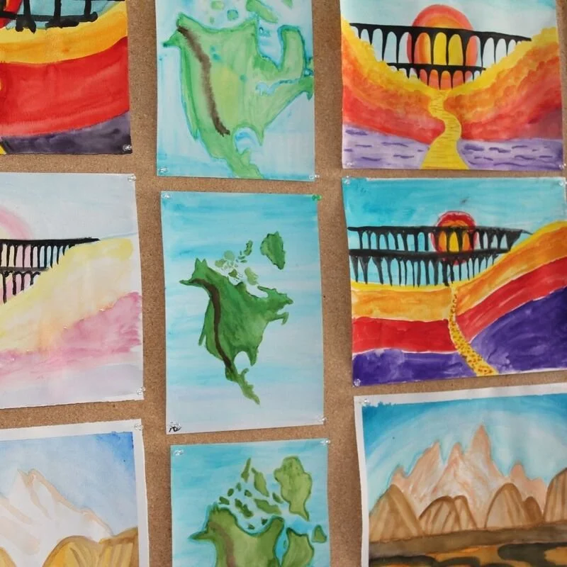 Series of watercolor paintings on display featuring landscapes, maps of Canada, and scenes of bridges, sunsets, and mountains.