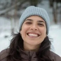 Smiling woman wearing a gray knit beanie and dark winter coat outdoors in a snowy setting