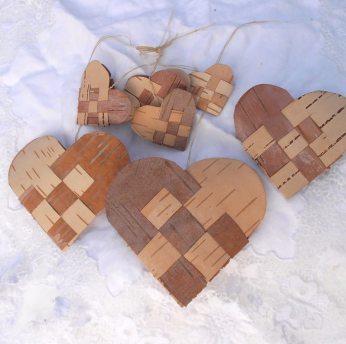 Six wooden heart-shaped ornaments with geometric patterns, laid on a textured white fabric.