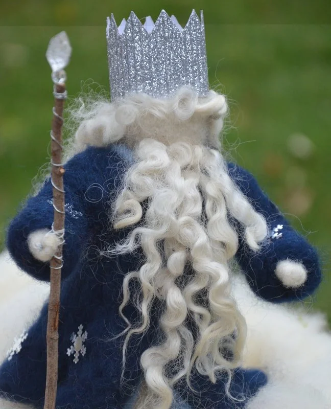 A plush toy of a king or wizard character with a white curly beard, wearing a silver paper crown, holding a staff, and dressed in a blue robe with snowflake decorations.