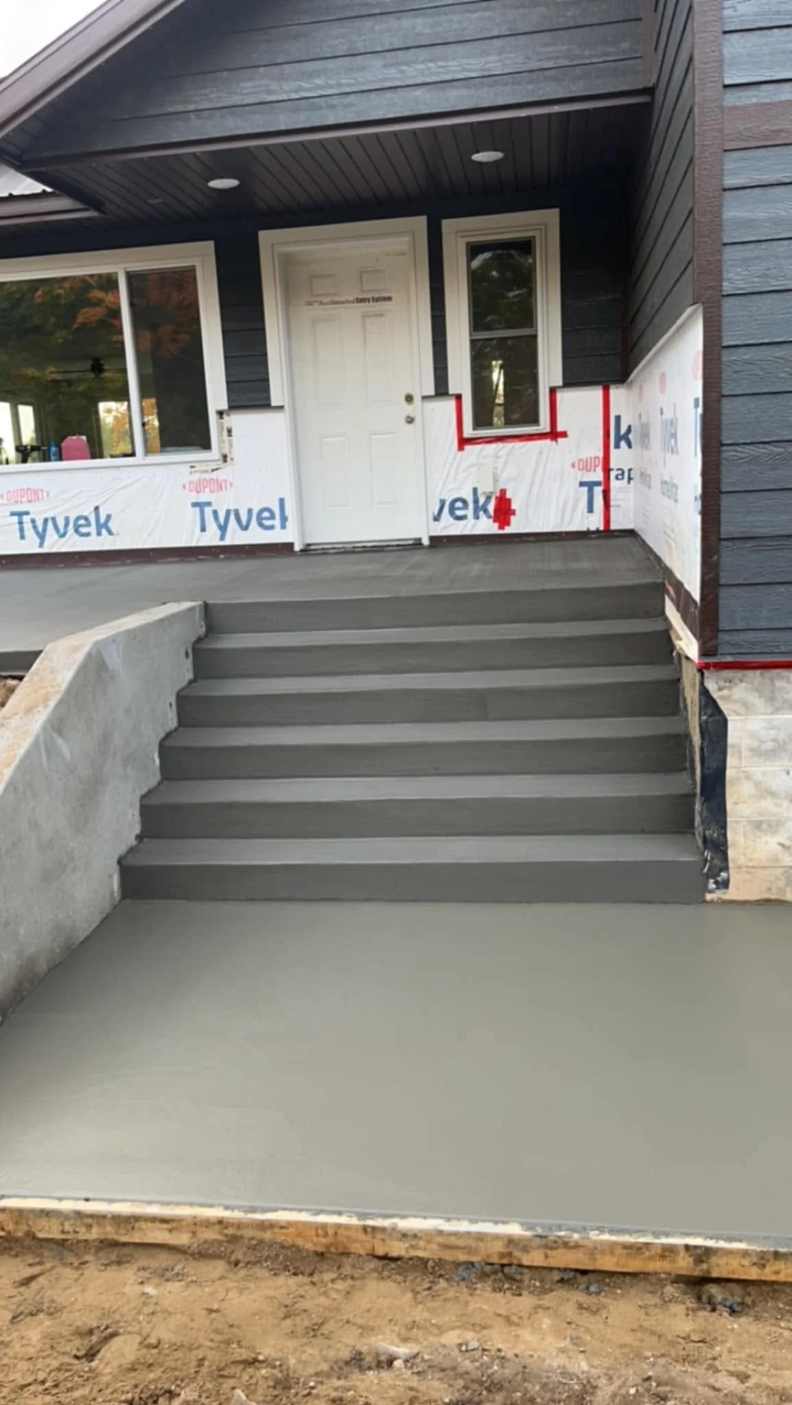 Newly poured concrete landing with stairs leading to a house entrance, with part of the house under construction visible.
