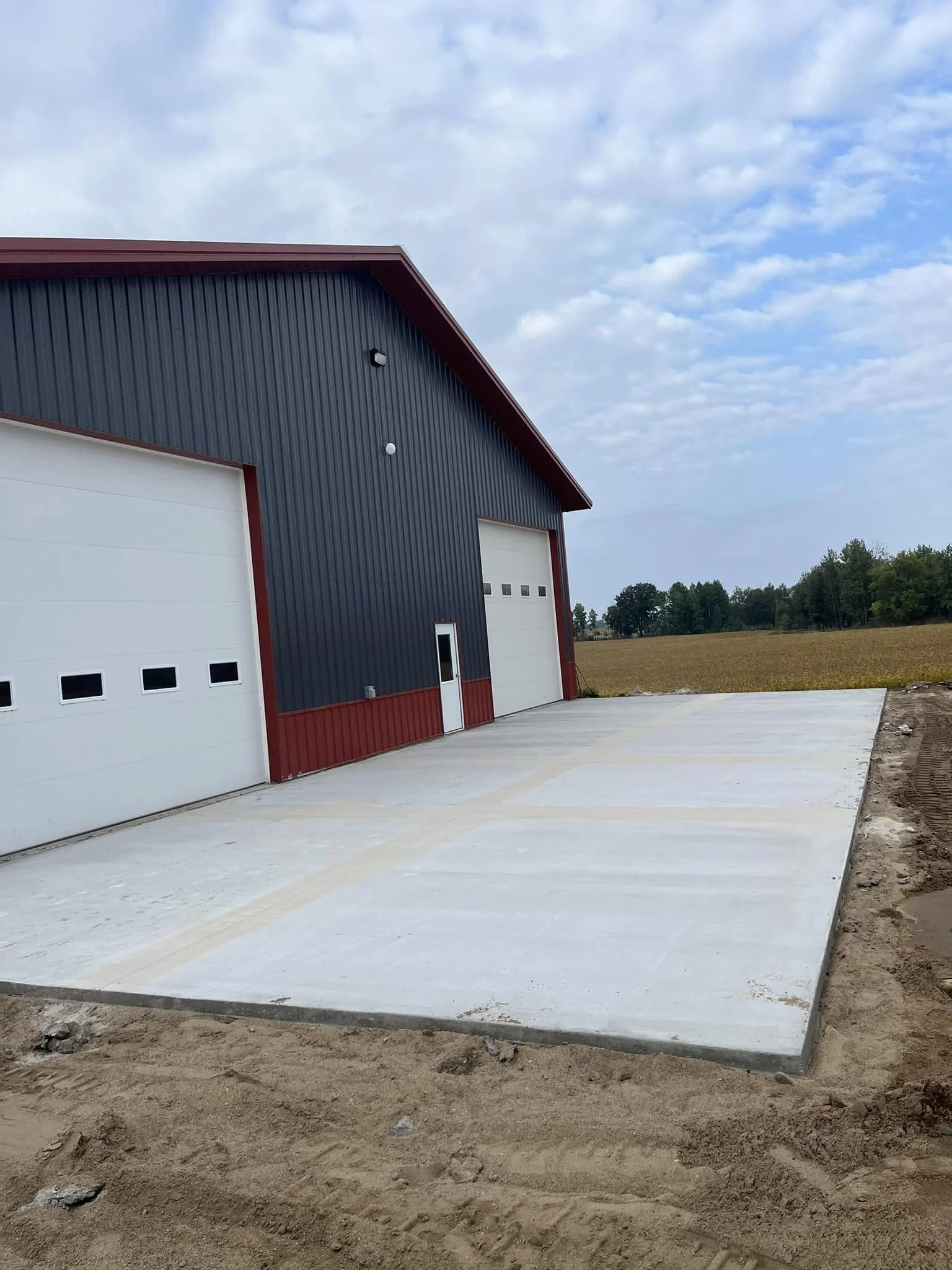 Newly poured concrete floor outside of a large industrial building with blue metal siding and large white doors, under partly cloudy sky.
