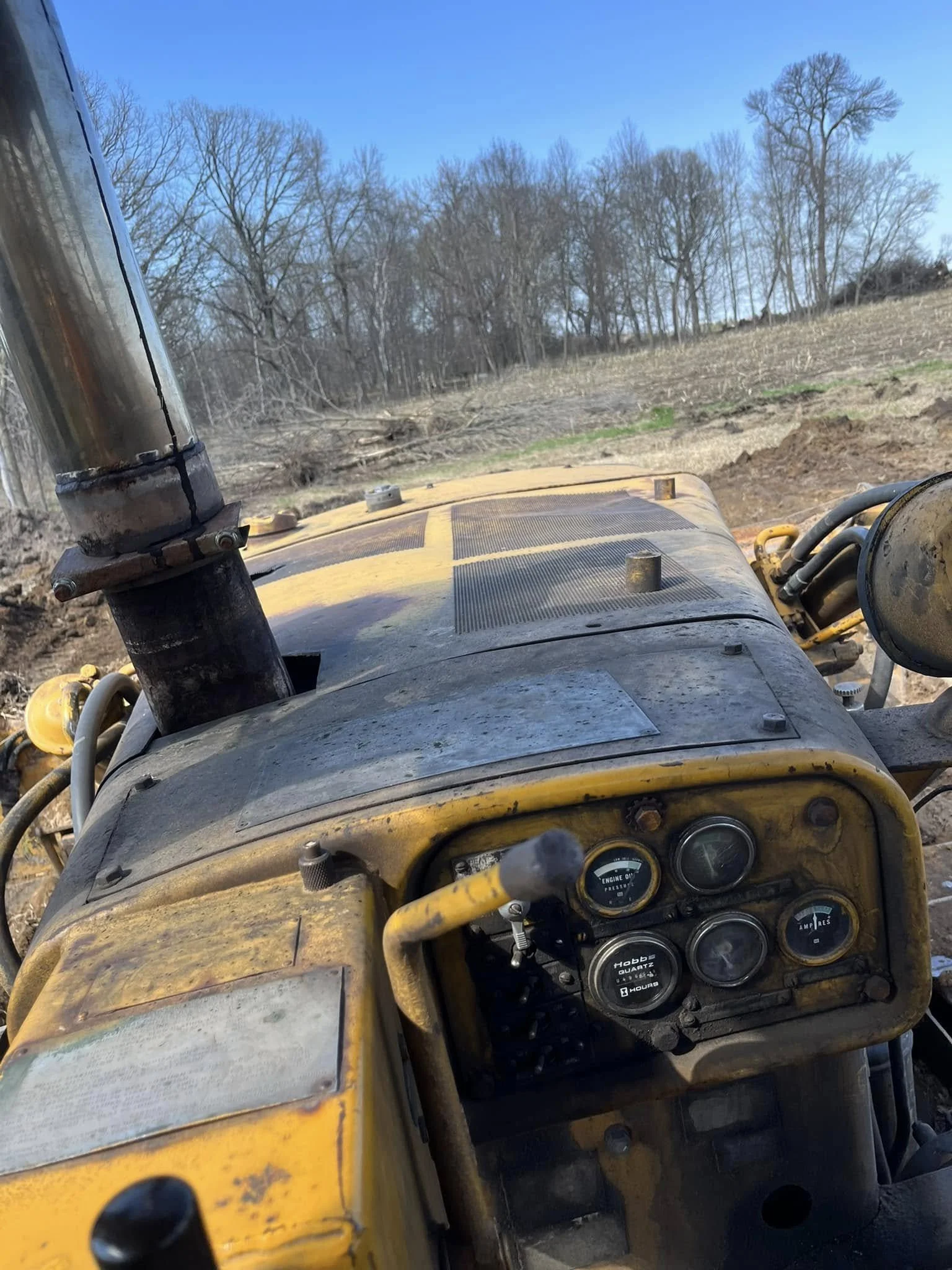 View from the driver's seat of a yellow off-road vehicle on a dirt trail with bare trees and a blue sky in the background.