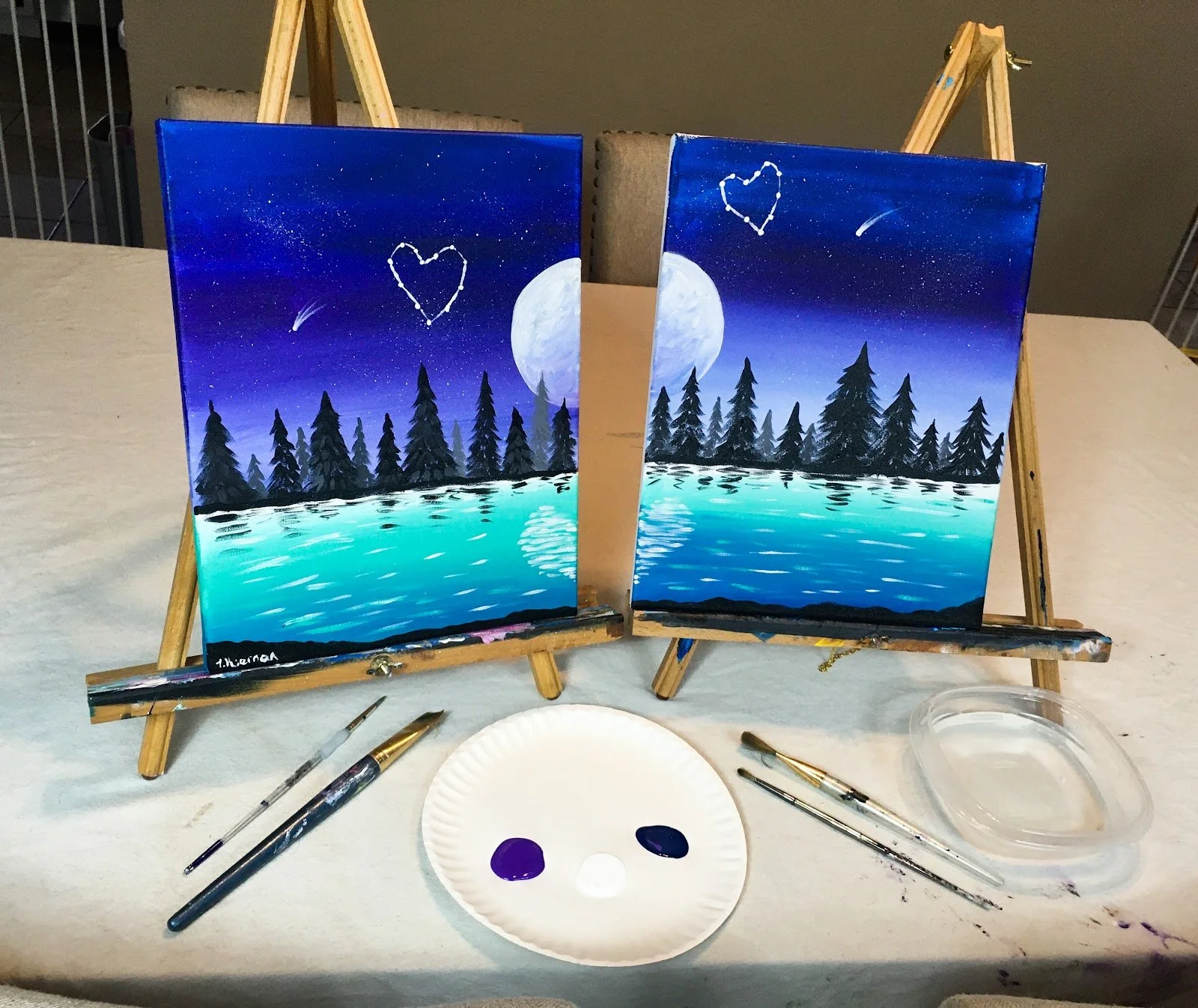 Two paintings of a night scene with a full moon, pine trees near a body of water, and a starry sky with a shooting star and a heart-shaped constellation.