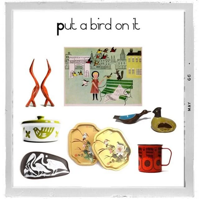 Artistic collection of decorative objects, including two orange twisted sculptures, a picture of a woman feeding birds in a city park, two bird figurines, a black and white swan dish, two yellow floral plates, and a red mug with a black pattern.