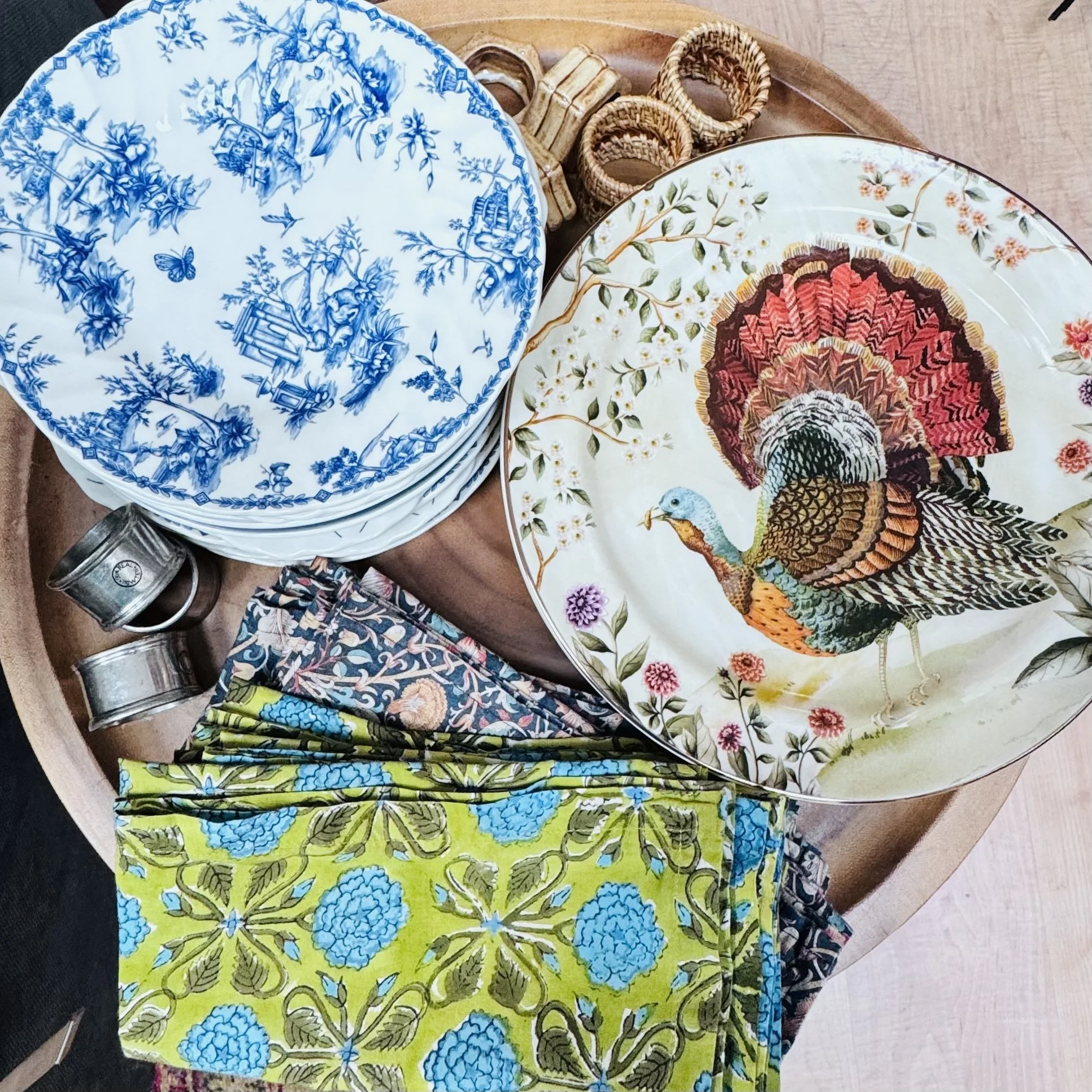 Colorful display of decorative ceramic plates with various floral and nature designs, arranged on a round wooden surface.
