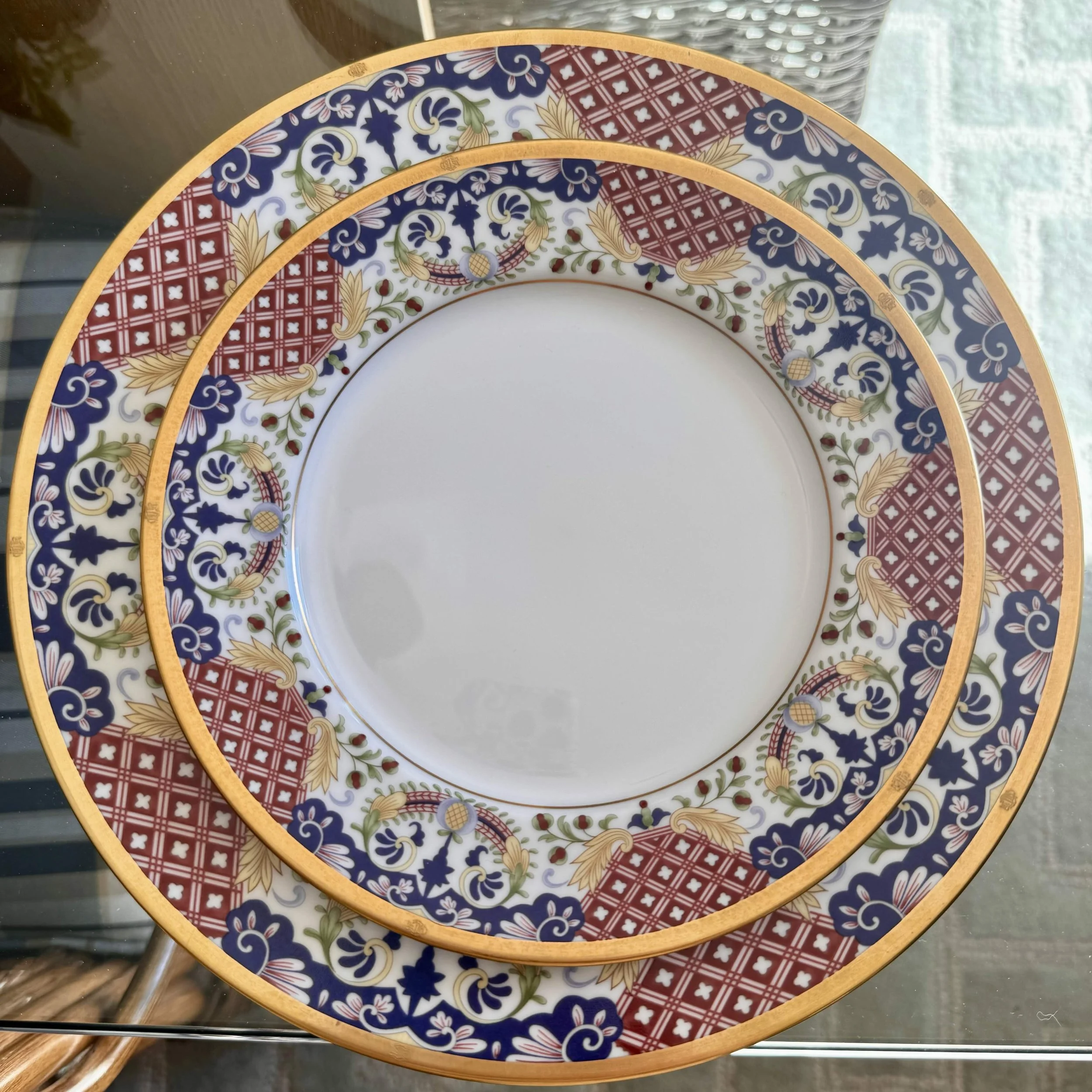 Close-up of two decorative ceramic plates with intricate blue, red, gold, and green floral and geometric patterns, stacked on a glass table.