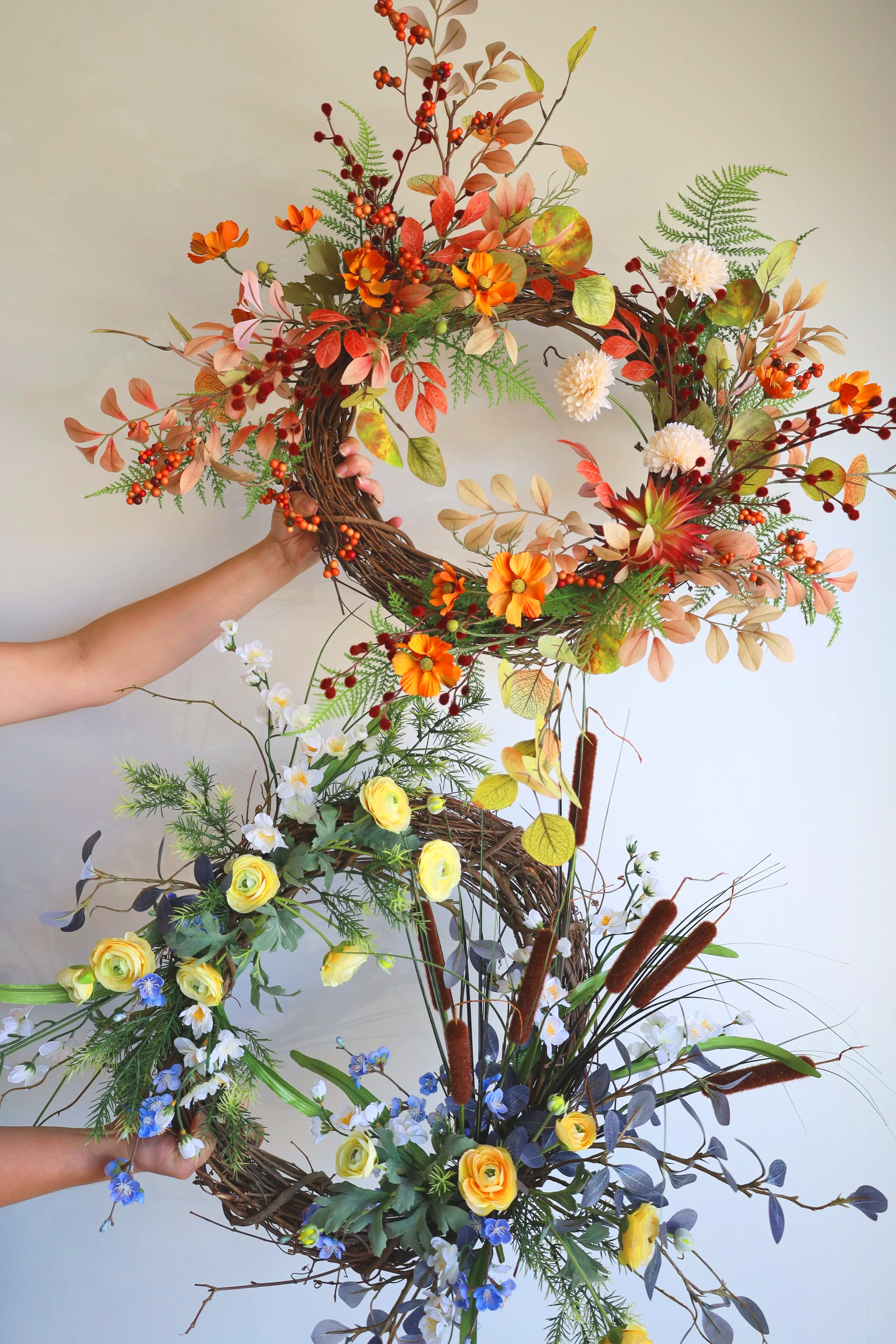 A decorative floral arrangement made of entwined branches and assorted colorful flowers including yellow roses, white daisies, orange and red blossoms, and green foliage.