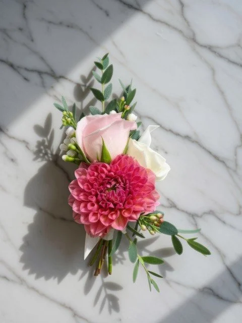 A boutonniere of pink and white flowers with green foliage placed on a marbled surface.