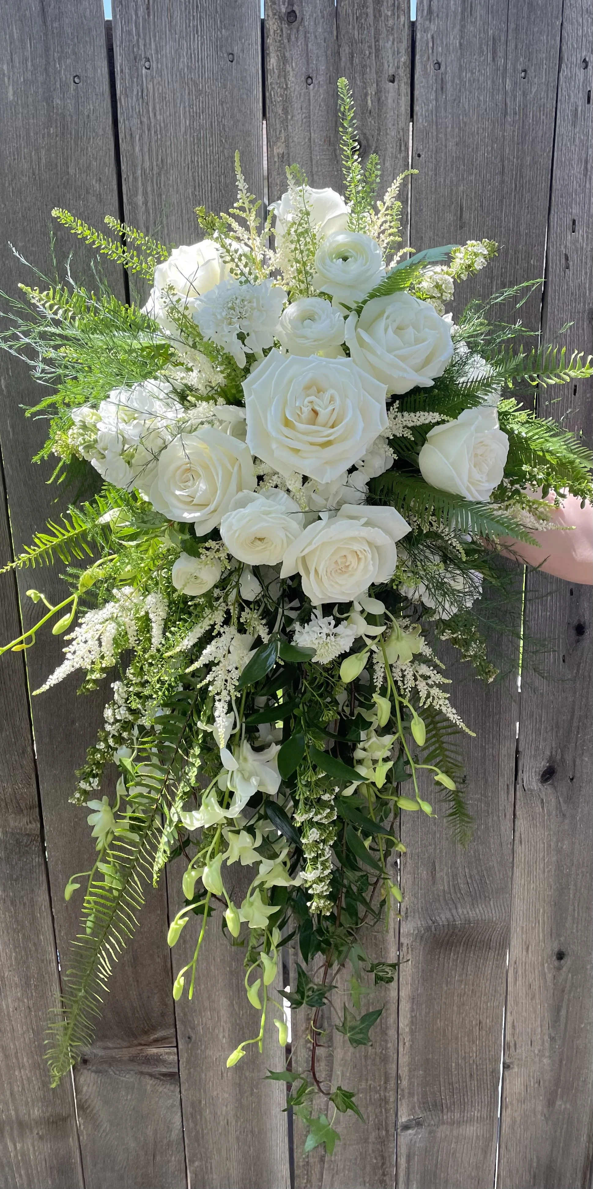 Cascading Bridal Bouquet of white roses, orchids, and greenery against a wooden background