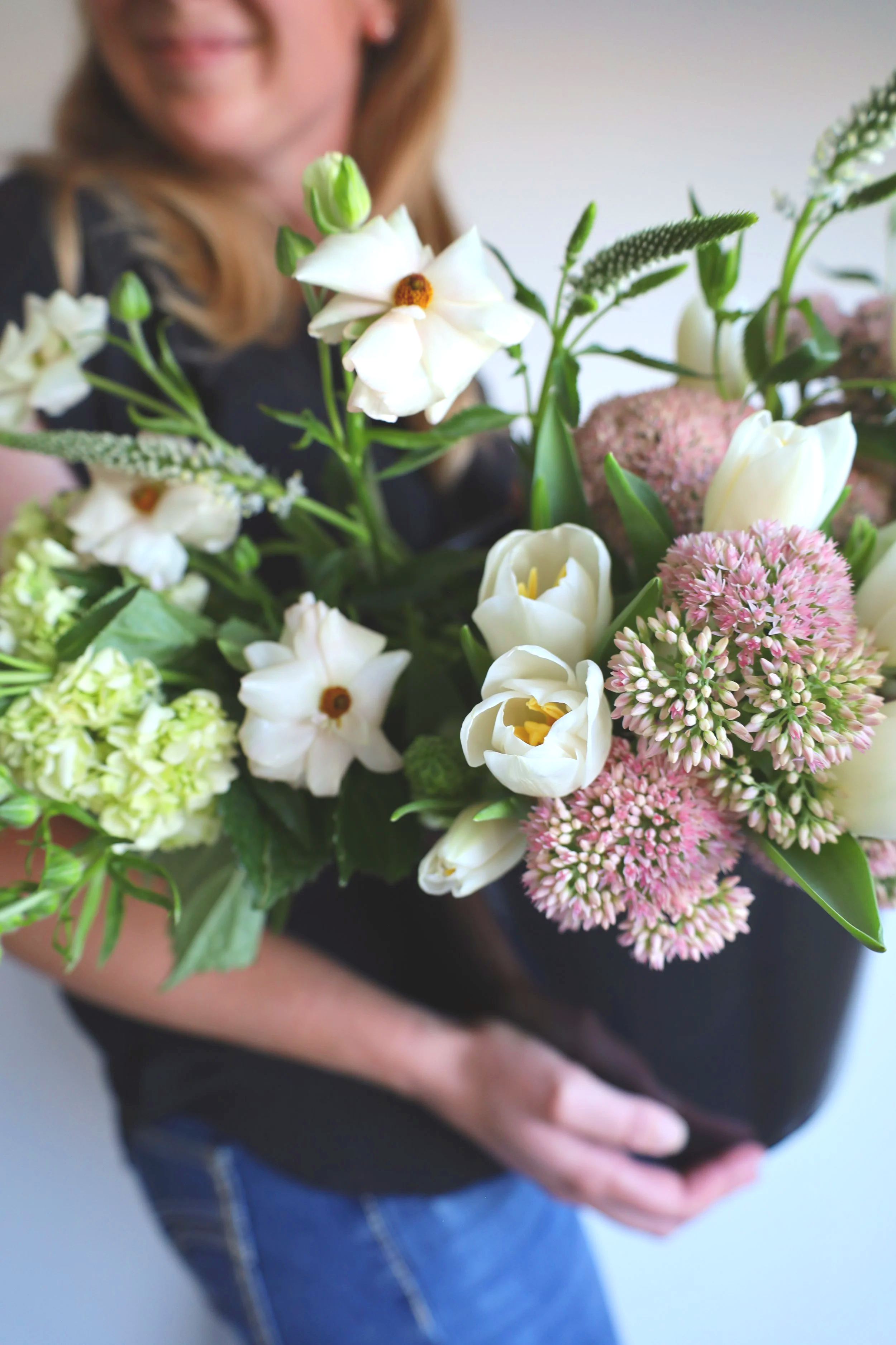 A person holding a bucket of white, pink, and green flowers against a plain background.