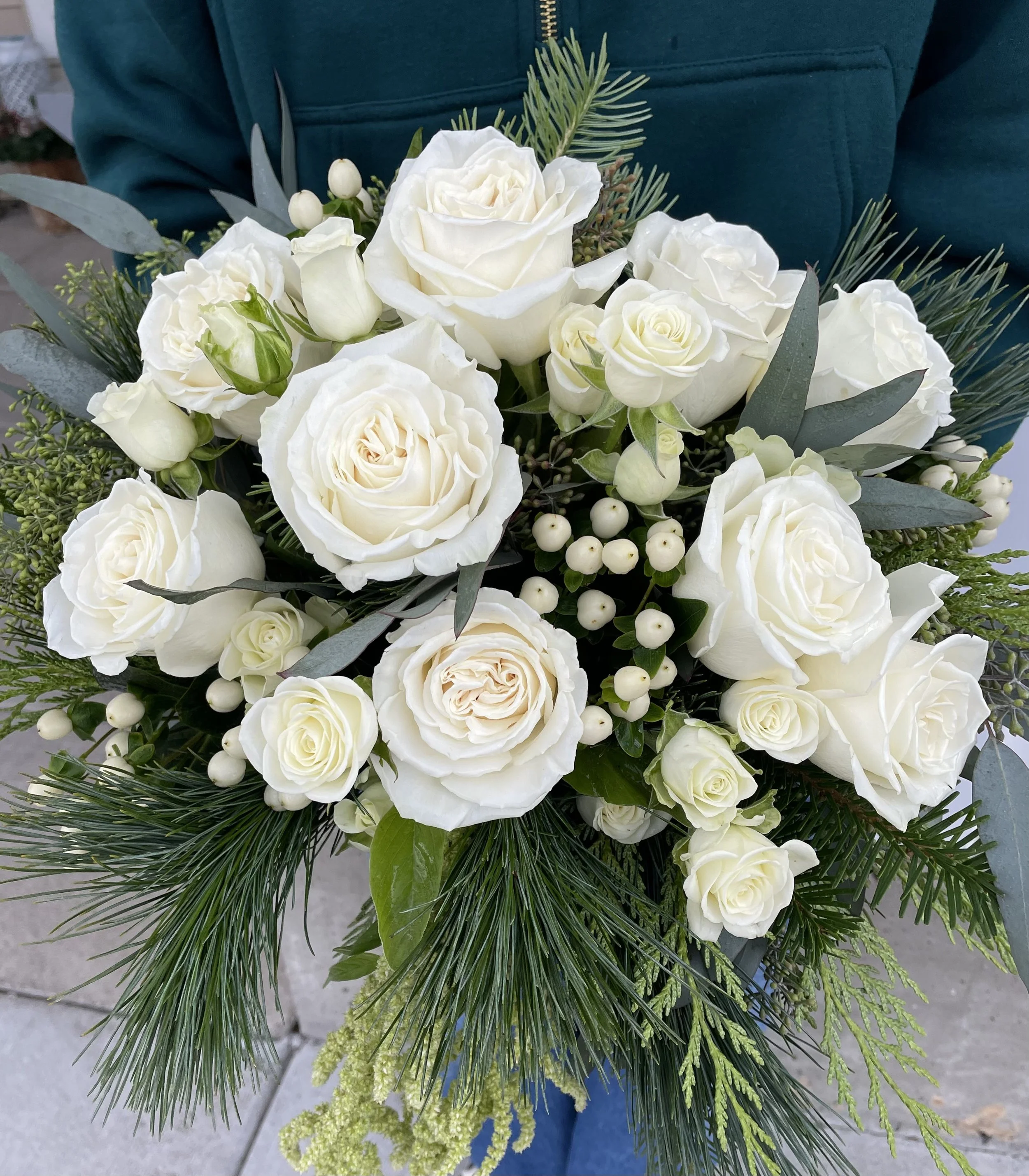 A bridal bouquet of white roses, Hypericum berries and greenery, including pine branches.