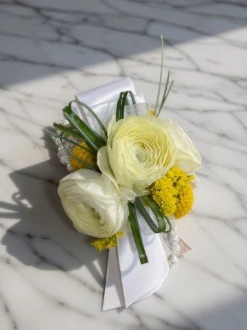 A wrist corsage with white ribbon and yellow flowers on a marble surface.