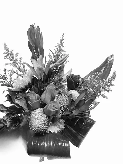 Black and white photograph of a tropical bouquet of flowers including roses and various greenery.