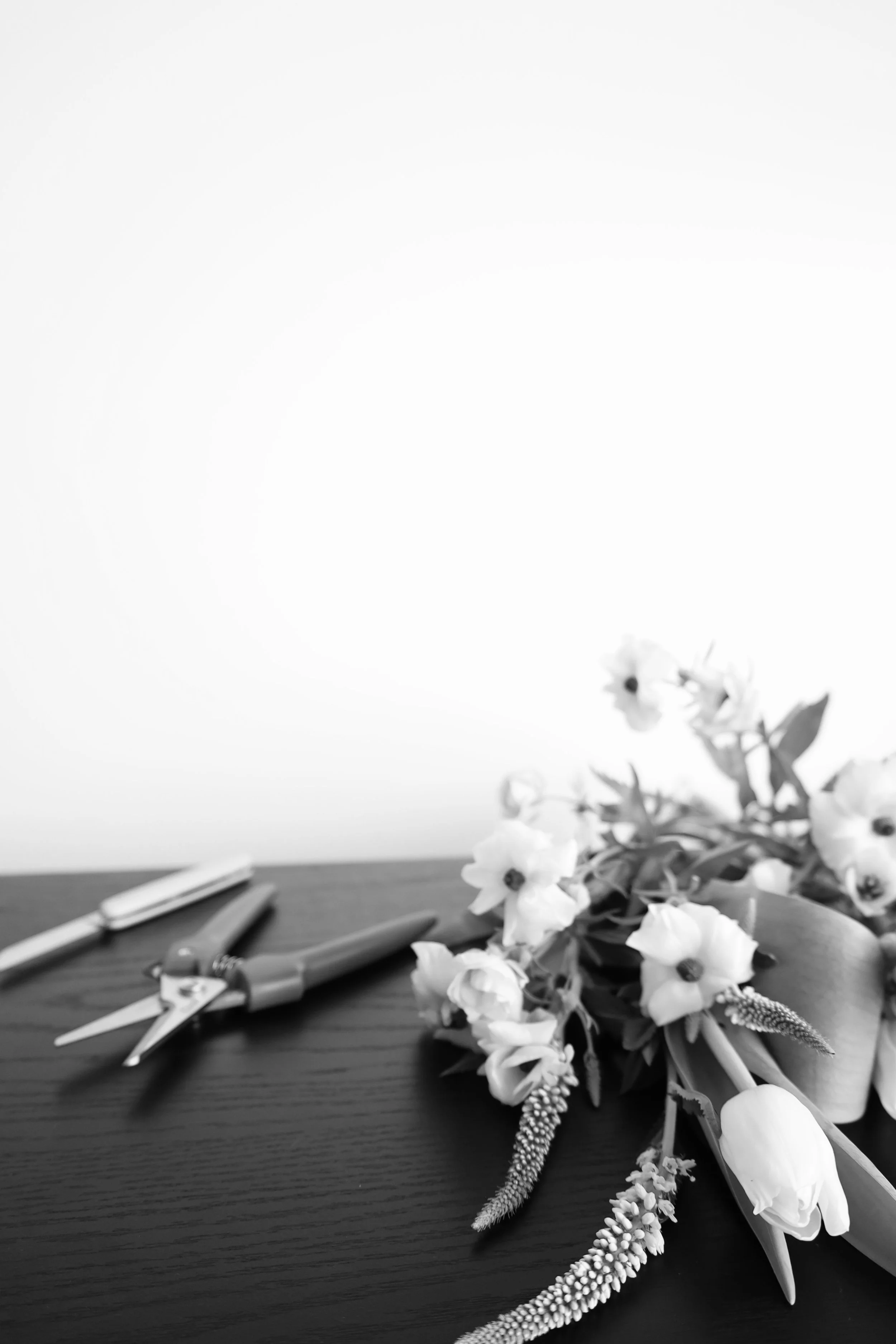 Black and white photo of a bouquet of flowers, and tools on a wooden table.