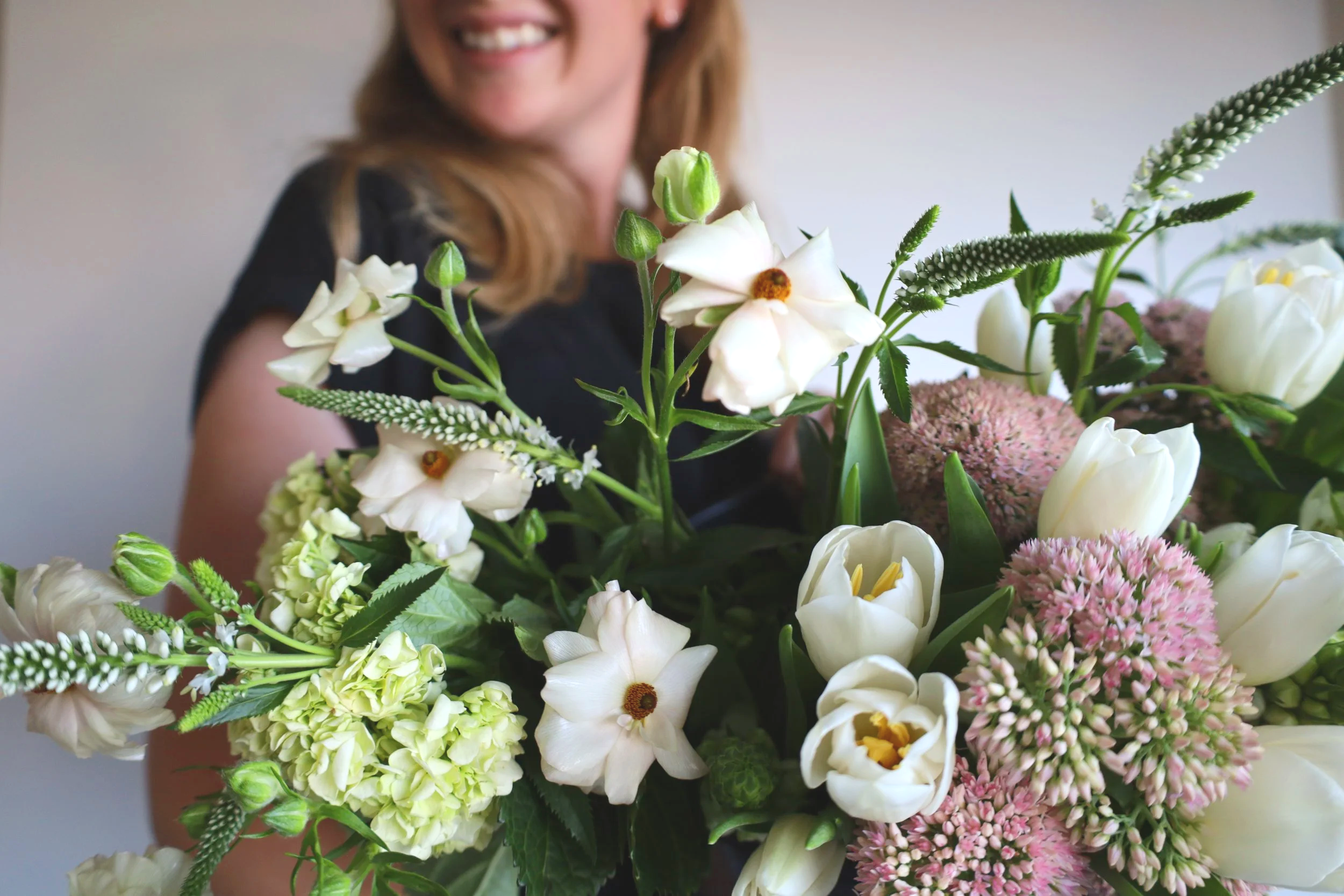A woman holding a large bouquet of white and pink flowers, smiling.