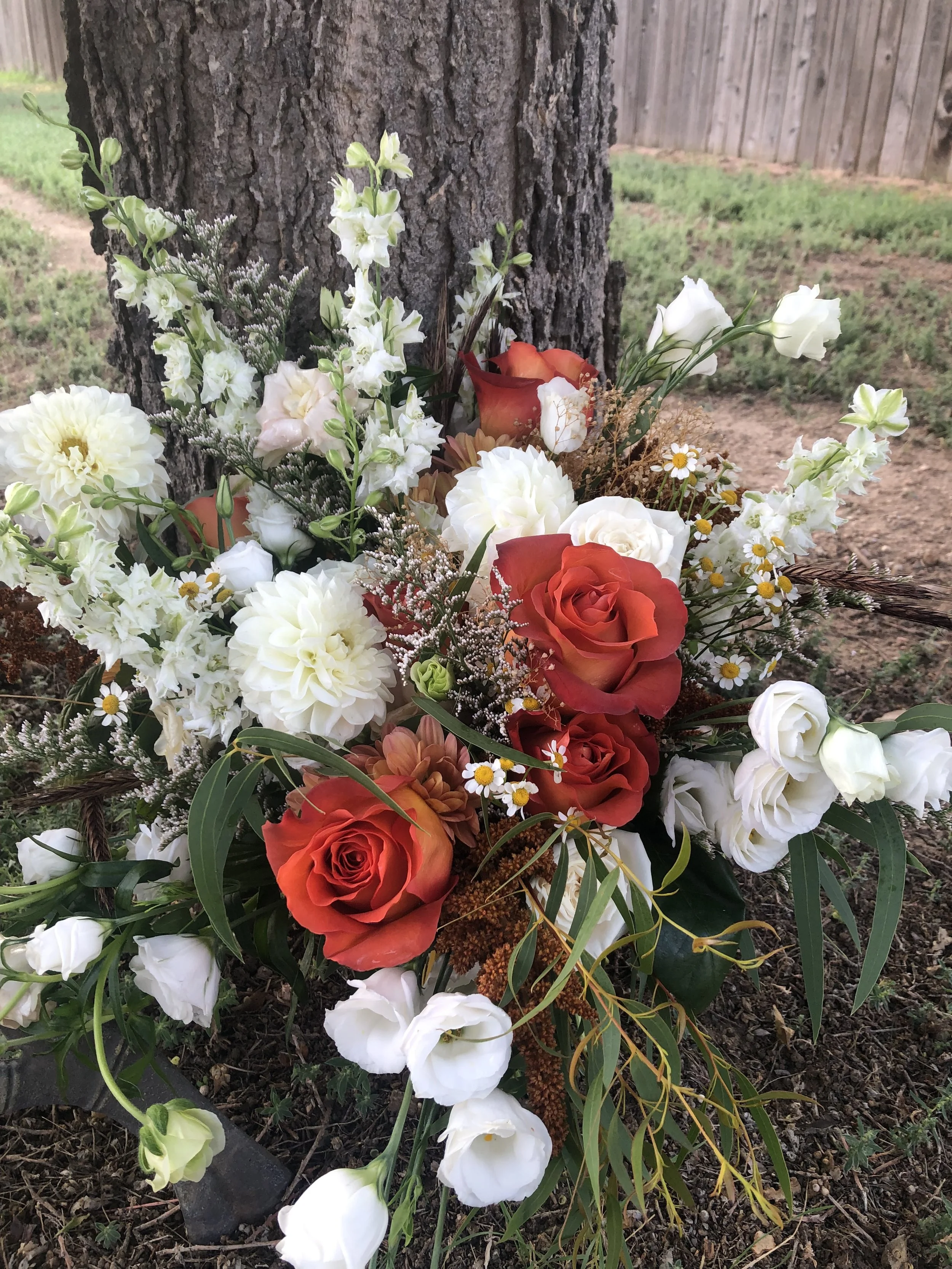 A rustic bridal bouquet of white and rust colored flowers with assorted greenery, placed against a tree trunk.