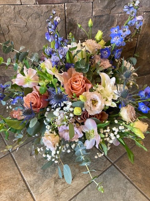 A colorful bridal bouquet with roses, delphiniums, and other mixed flowers against a stone wall background.