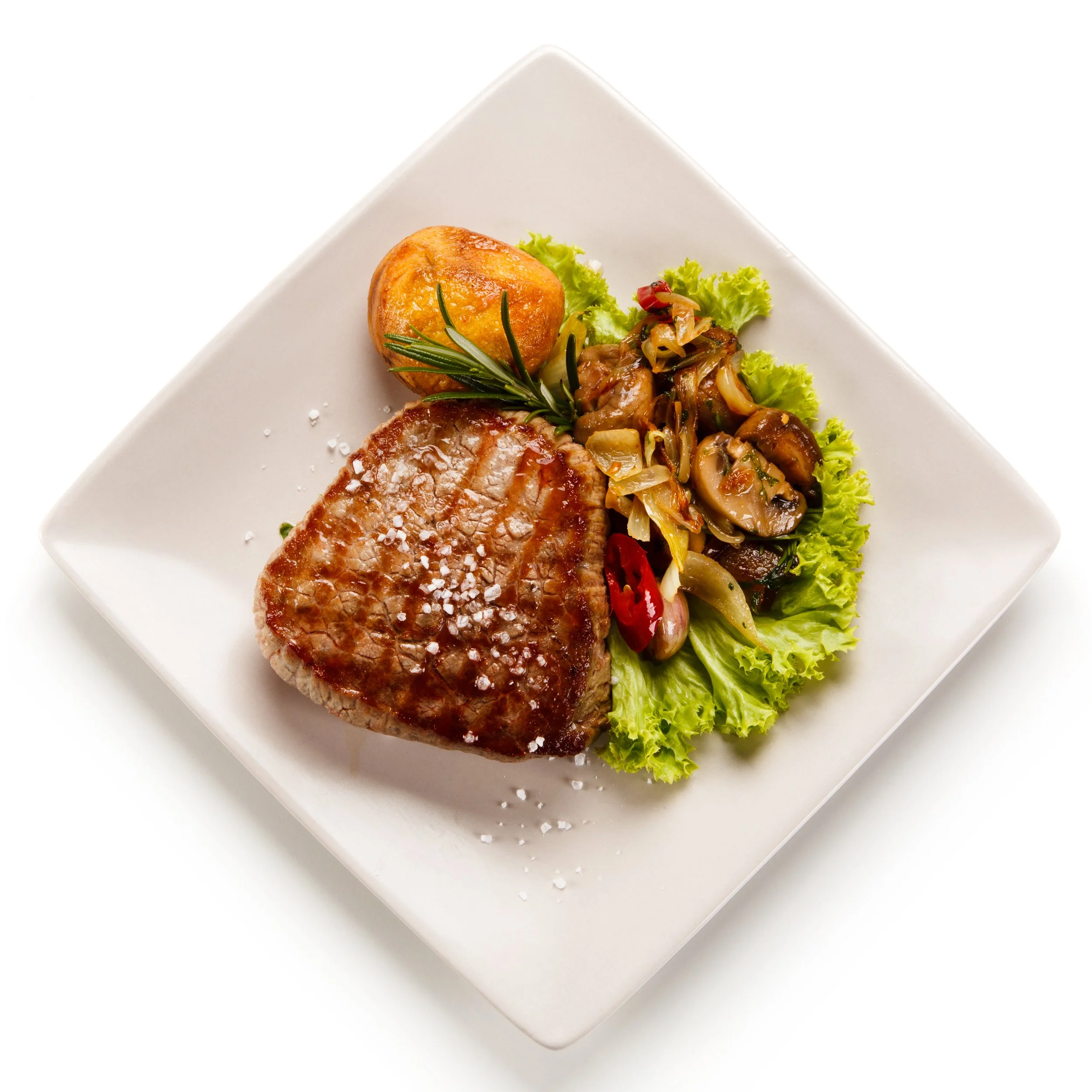 Close-up of a white square plate with a cooked steak, a baked potato garnished with herbs, and a small salad with lettuce and onions.