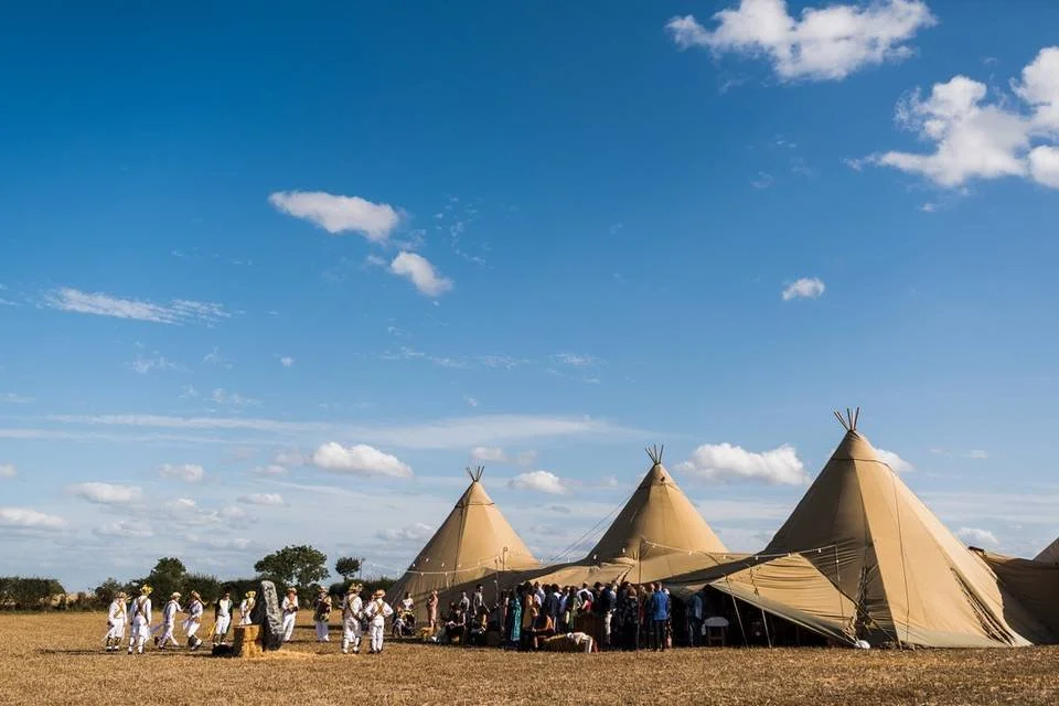 Halfmoon Farm, Hambleton with a group of Native Americans standing and sitting outside large teepees under a partly cloudy sky.