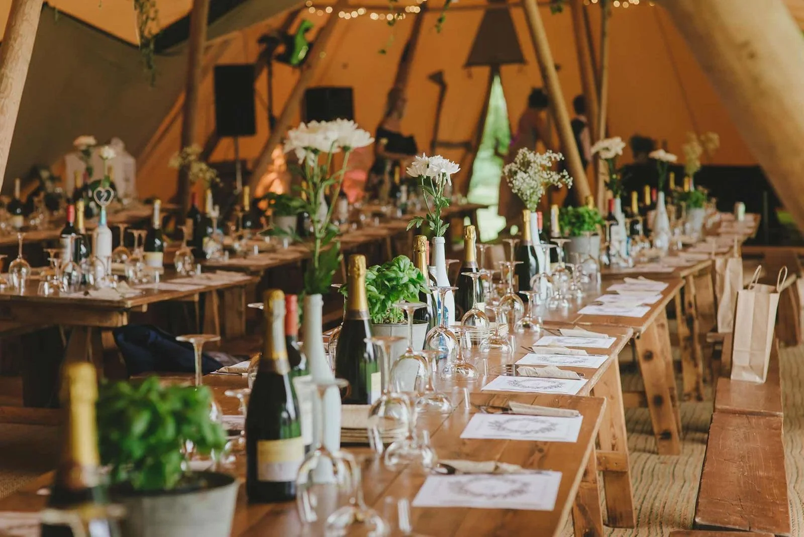 The Granary with a long rustic banquet table in a decorated tent, set with bottles of champagne, wine, green plants, flowers, wine glasses, and place settings for an event.