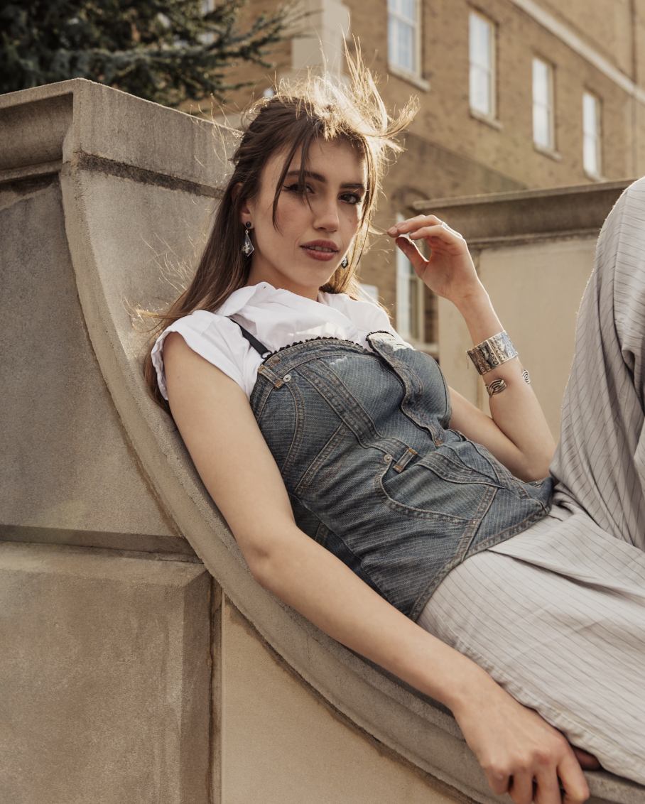 Fashion portrait of a woman in denim overalls reclining on a stone ledge outdoors