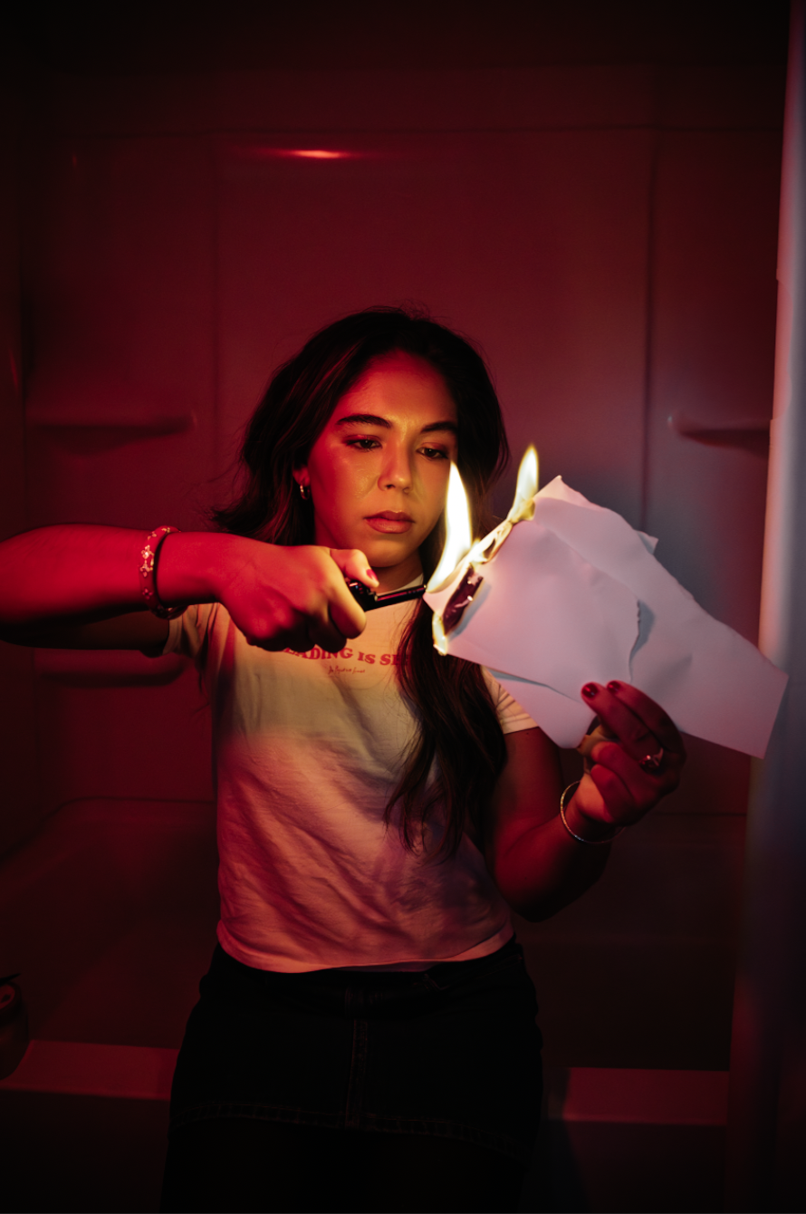 Woman using scissors to cut a flaming sheet of paper under dramatic red lighting