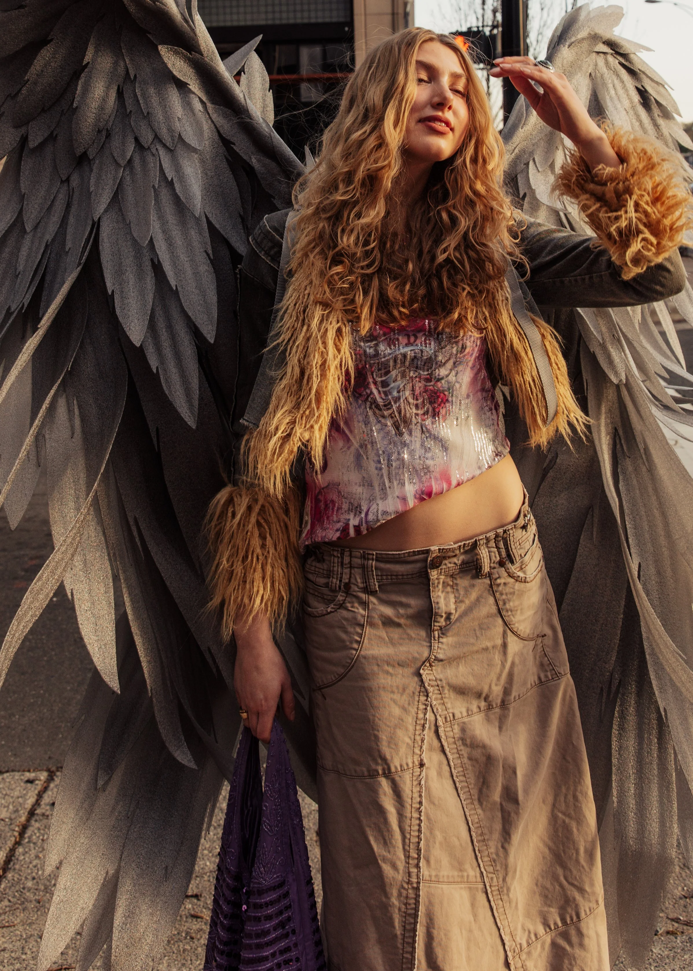 Woman with long curly hair posing in front of large gray angel wings