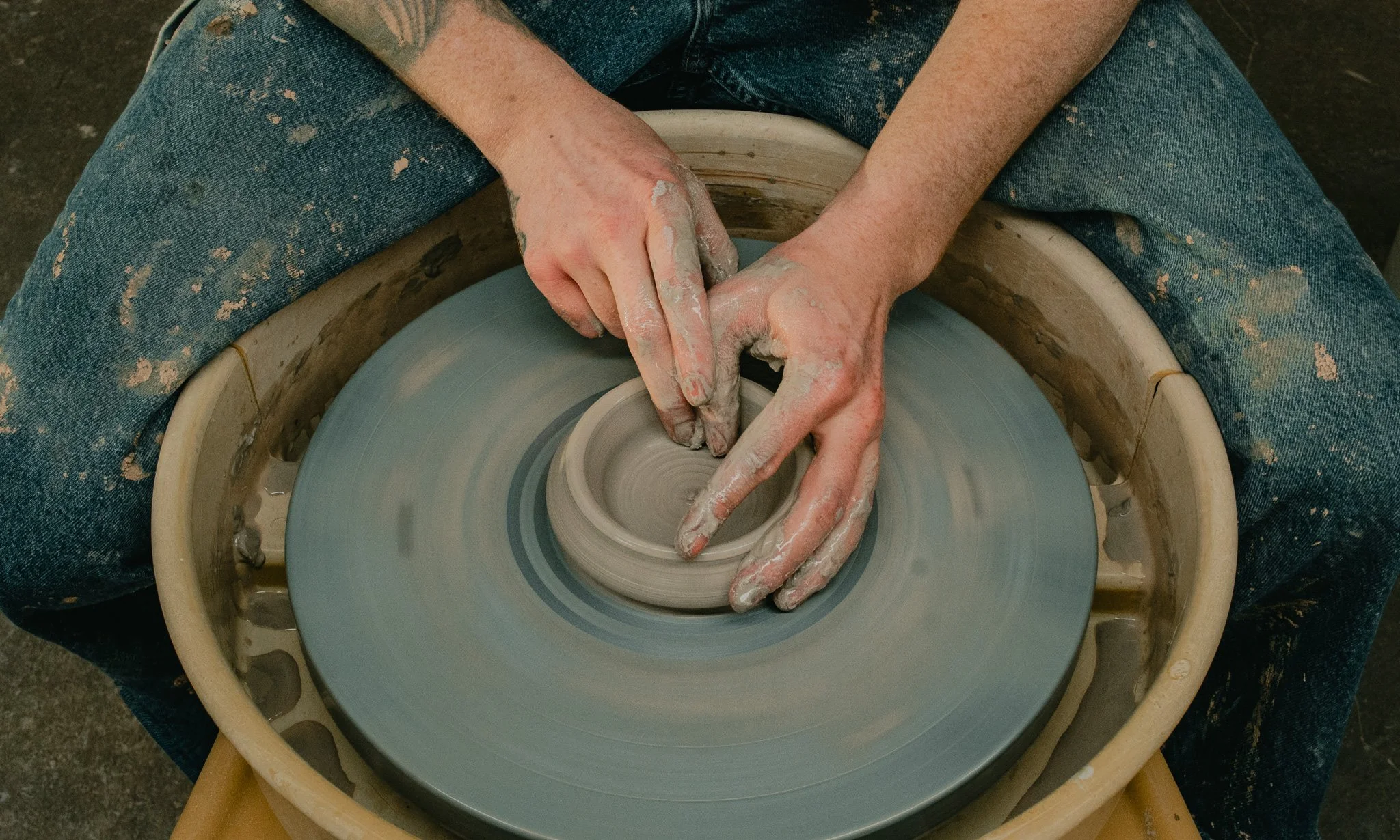 Potter shaping clay on a spinning pottery wheel with clay-covered hands