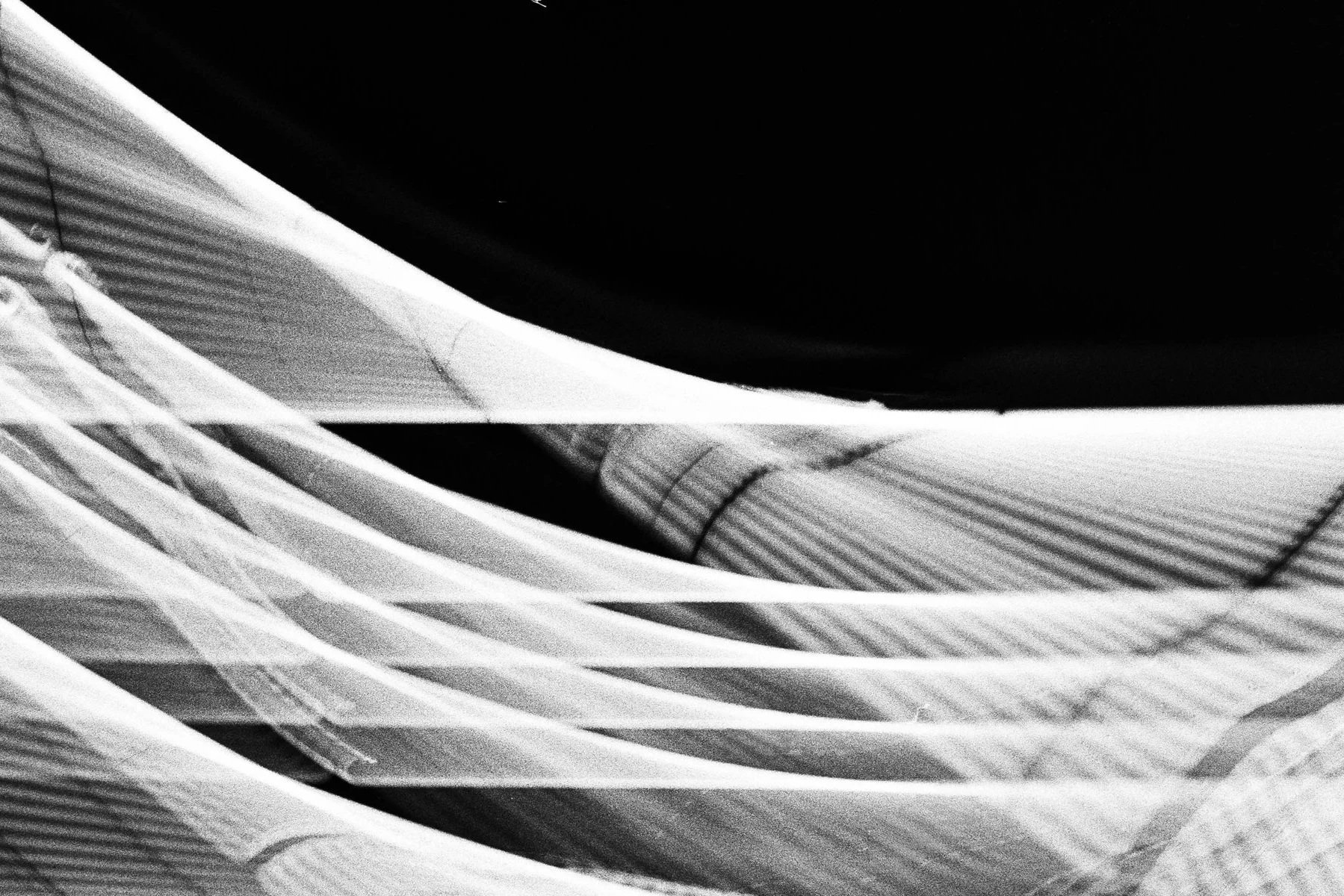 Black-and-white close-up of overlapping folded fabric with visible seams and striped texture
