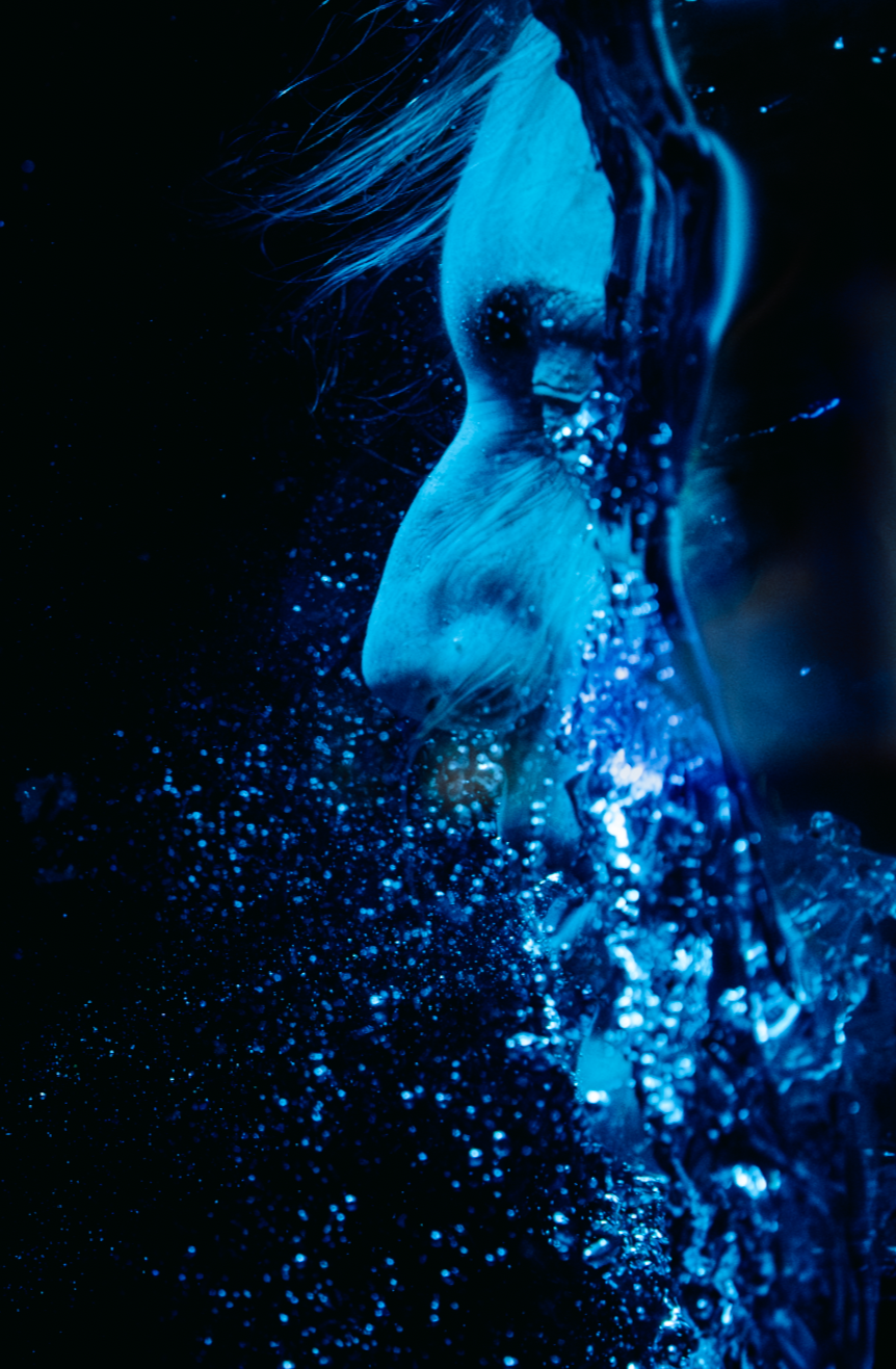 Close-up side profile of a woman underwater with flowing hair and bubbles illuminated in blue light