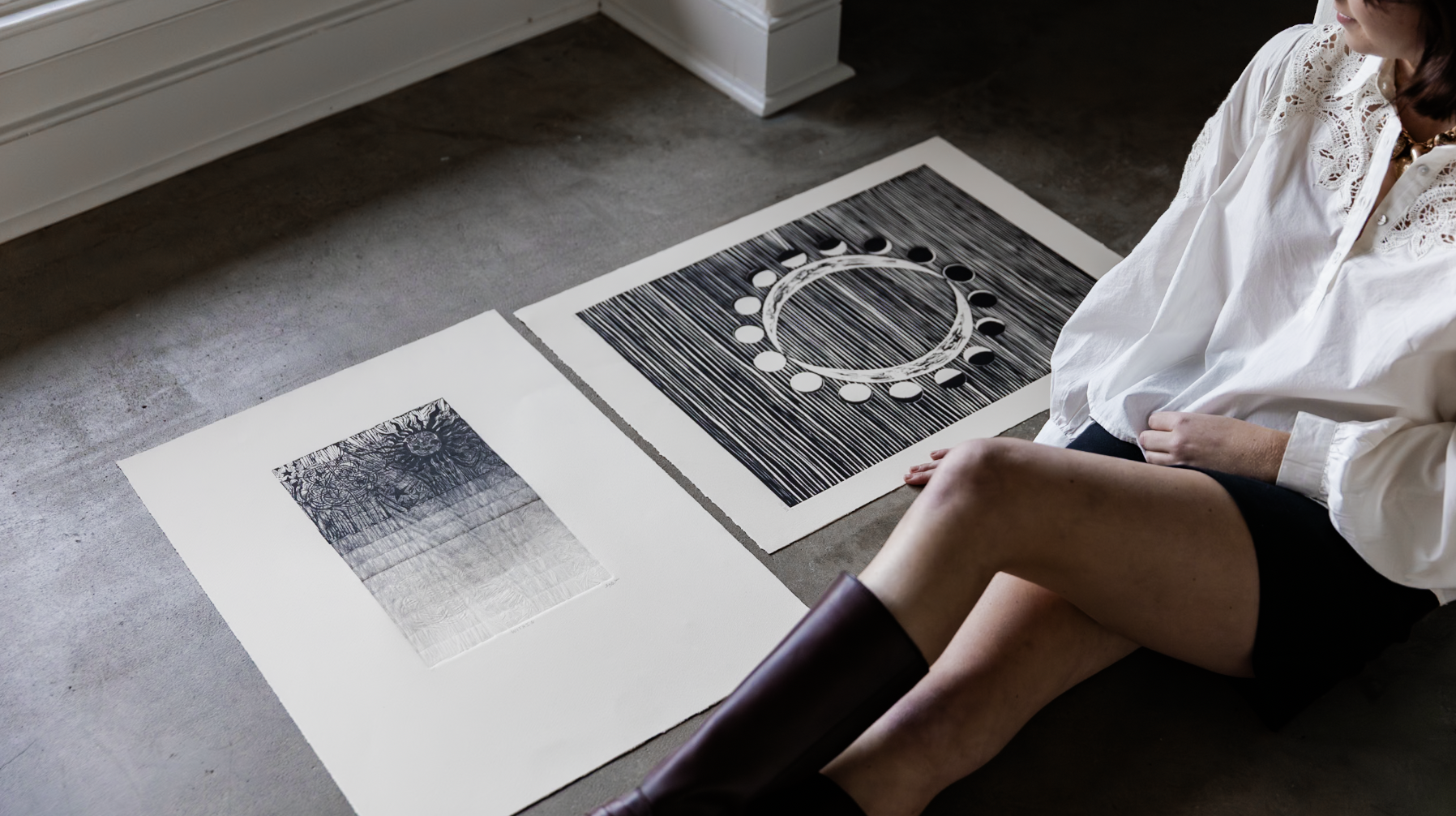 Woman sitting beside two large black-and-white art prints on a concrete floor