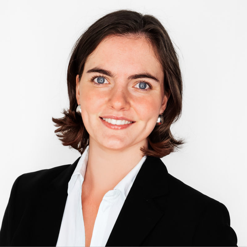 Smiling professional woman with short brown hair wearing a black blazer and white blouse against a white background