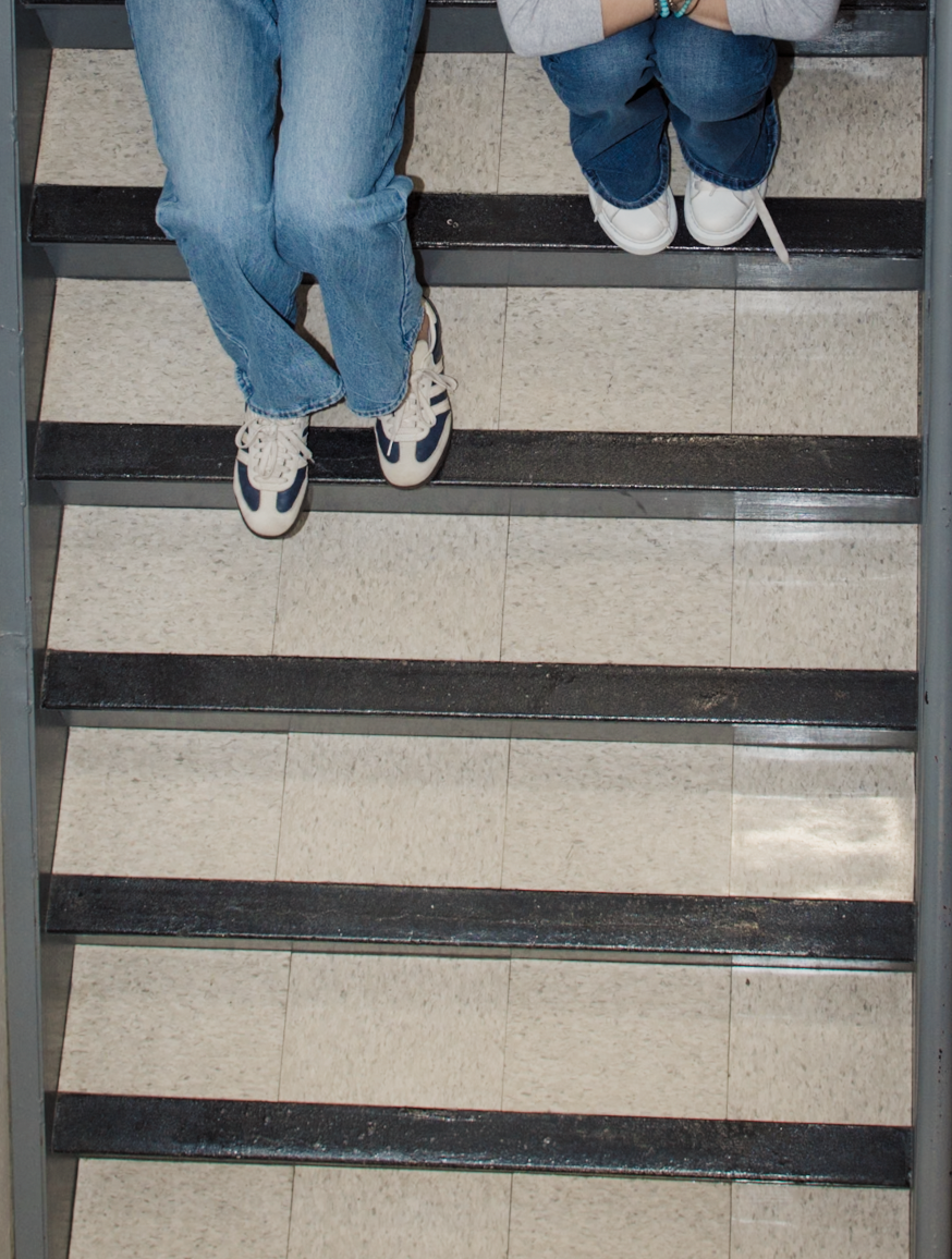 Top-down view of two people’s legs and sneakers on indoor tiled stairs