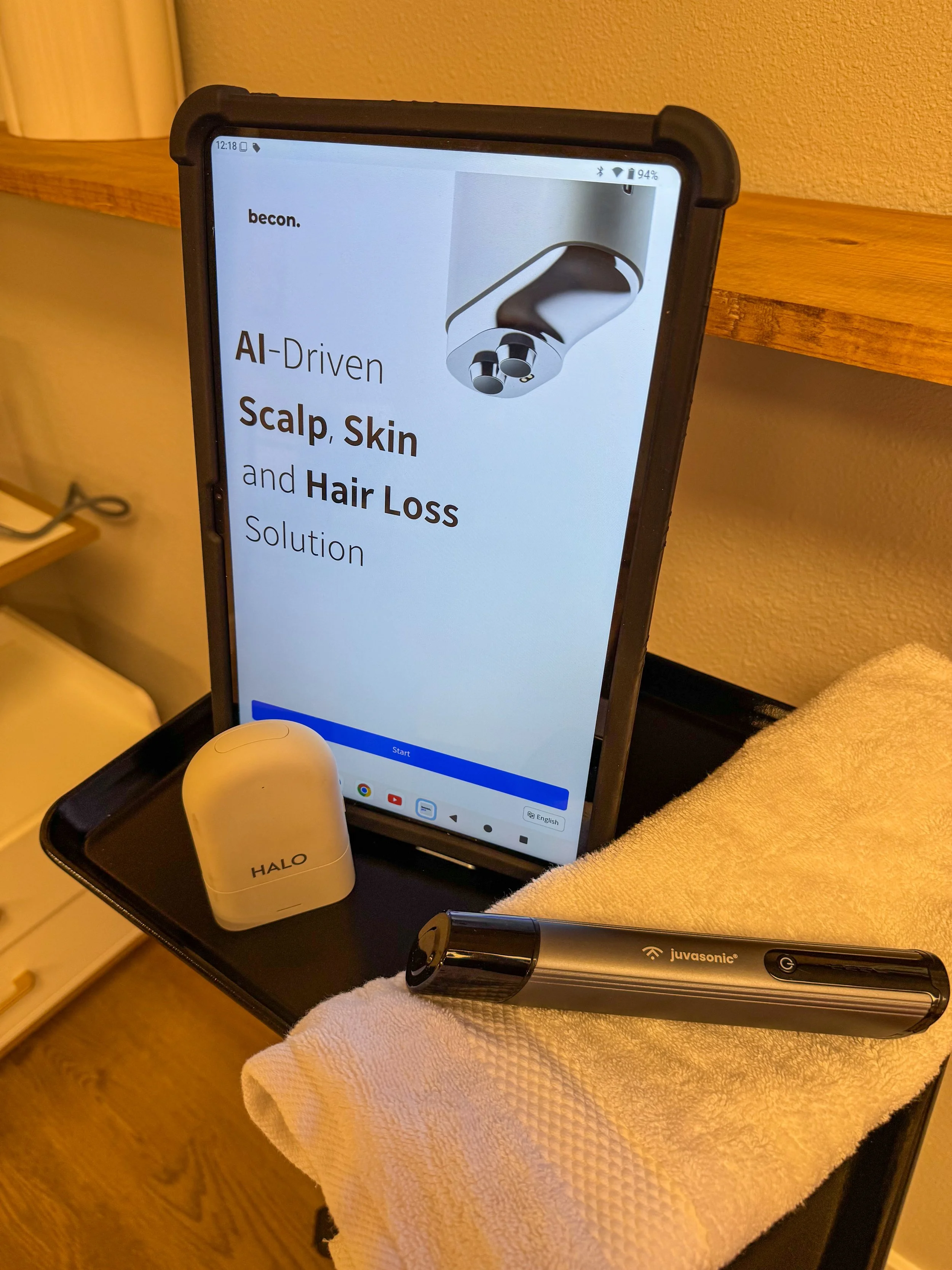 A tablet on a black tray displays an advertisement for AI-driven scalp, skin, and hair loss solutions, with a device and a small white rounded object labeled 'HALO' nearby.