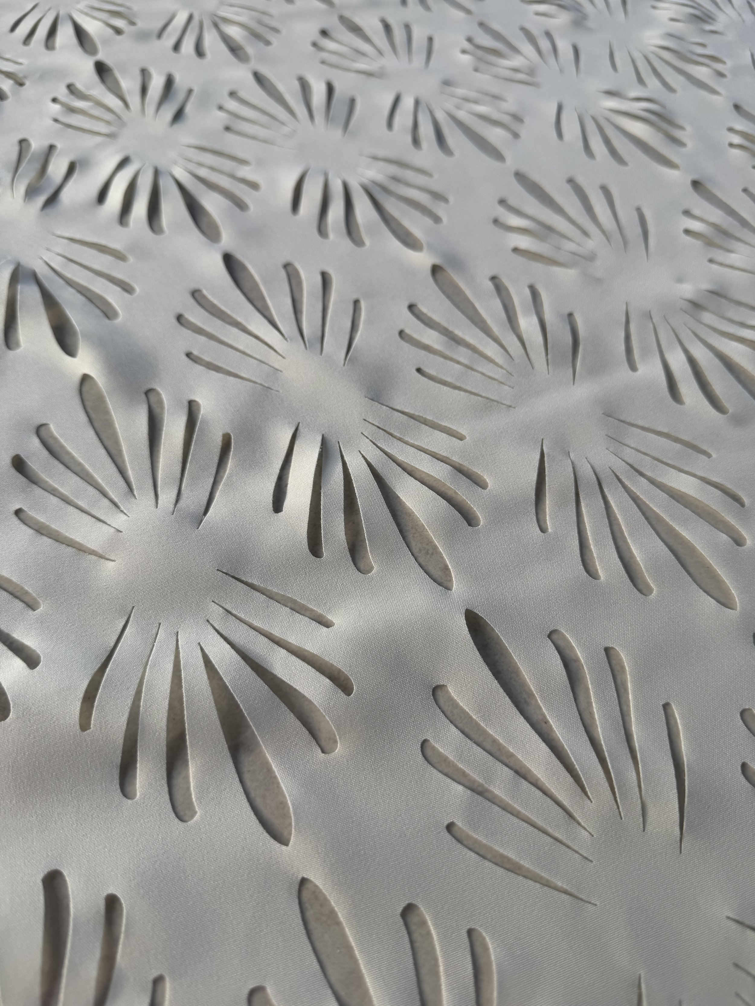 Close-up of a decorative surface with a pattern of stylized flowers and leaves cut out of a material, likely metal or plastic.