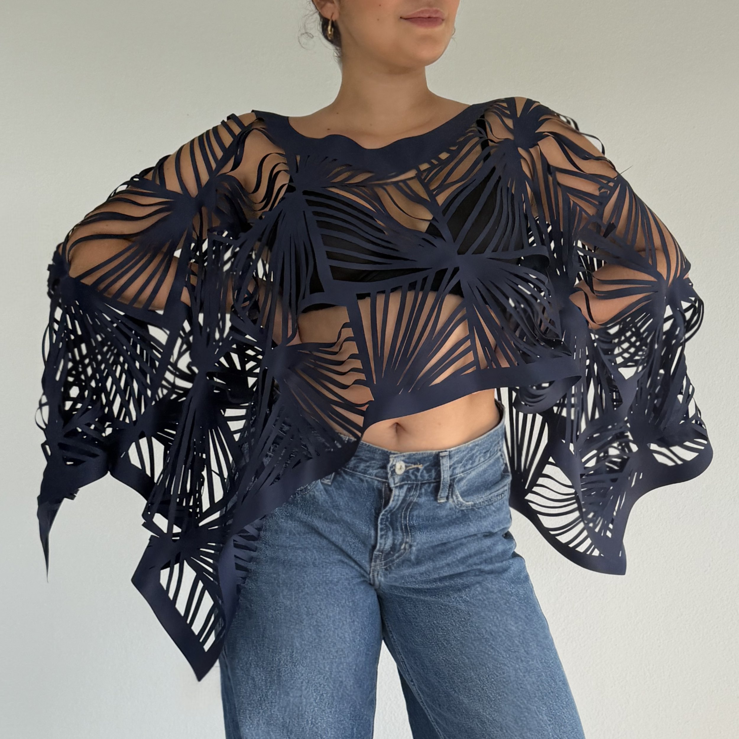A woman wearing a stylish navy blue top with cut-out leaf pattern and blue jeans against a light background.
