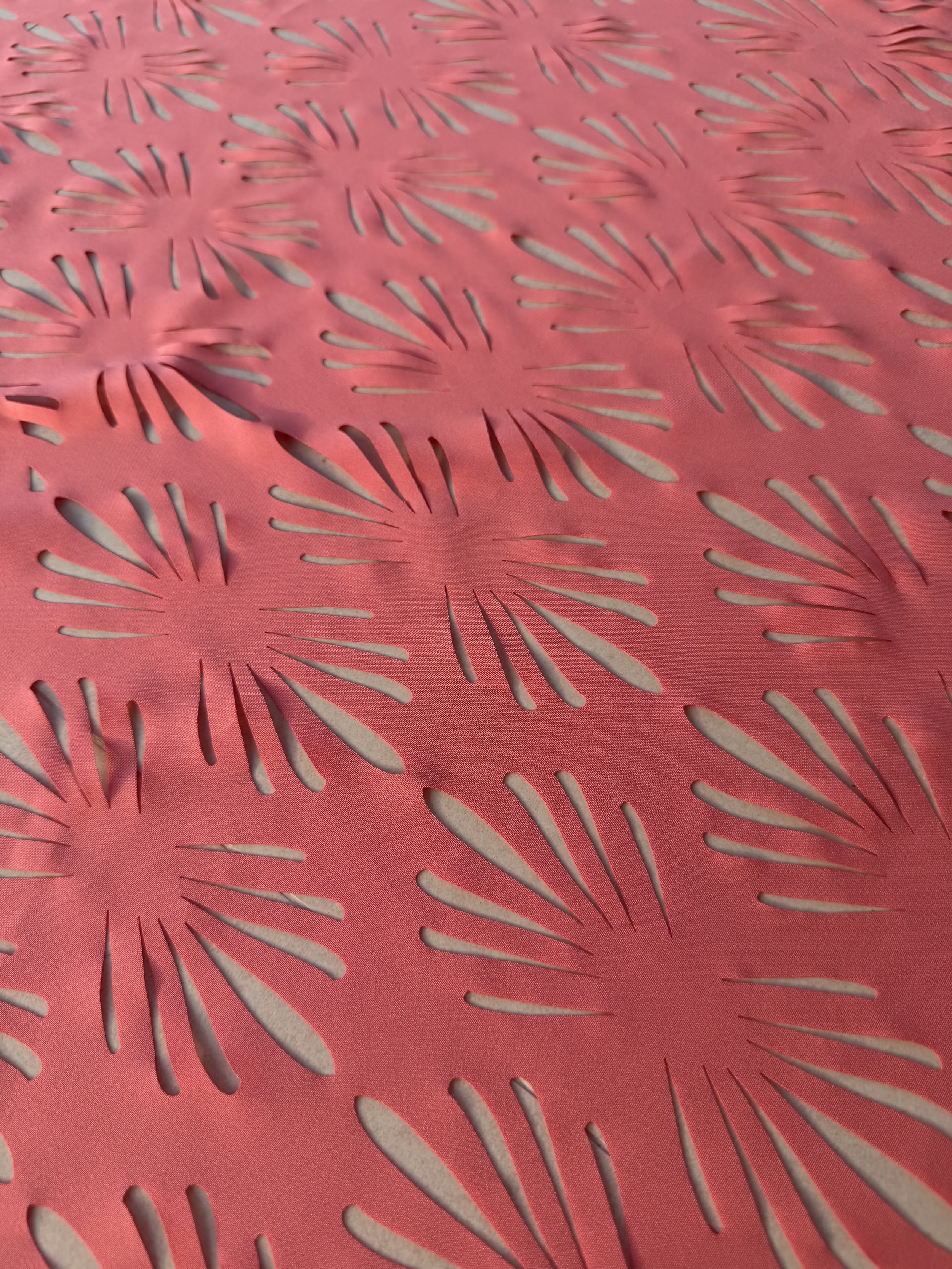 Close-up view of a pink paper or fabric with cut-out designs resembling sunbursts or flower shapes.