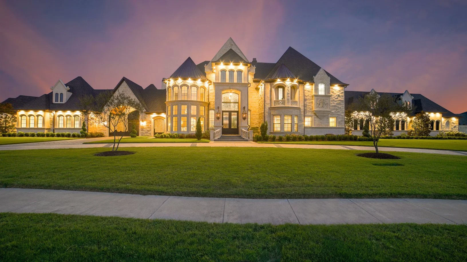 An example of Large, ornate mansion with stone and stucco exterior, illuminated by exterior lights at dusk, surrounded by a neatly manicured lawn and minimal landscaping that New Jersey used for property tax consulting works example.