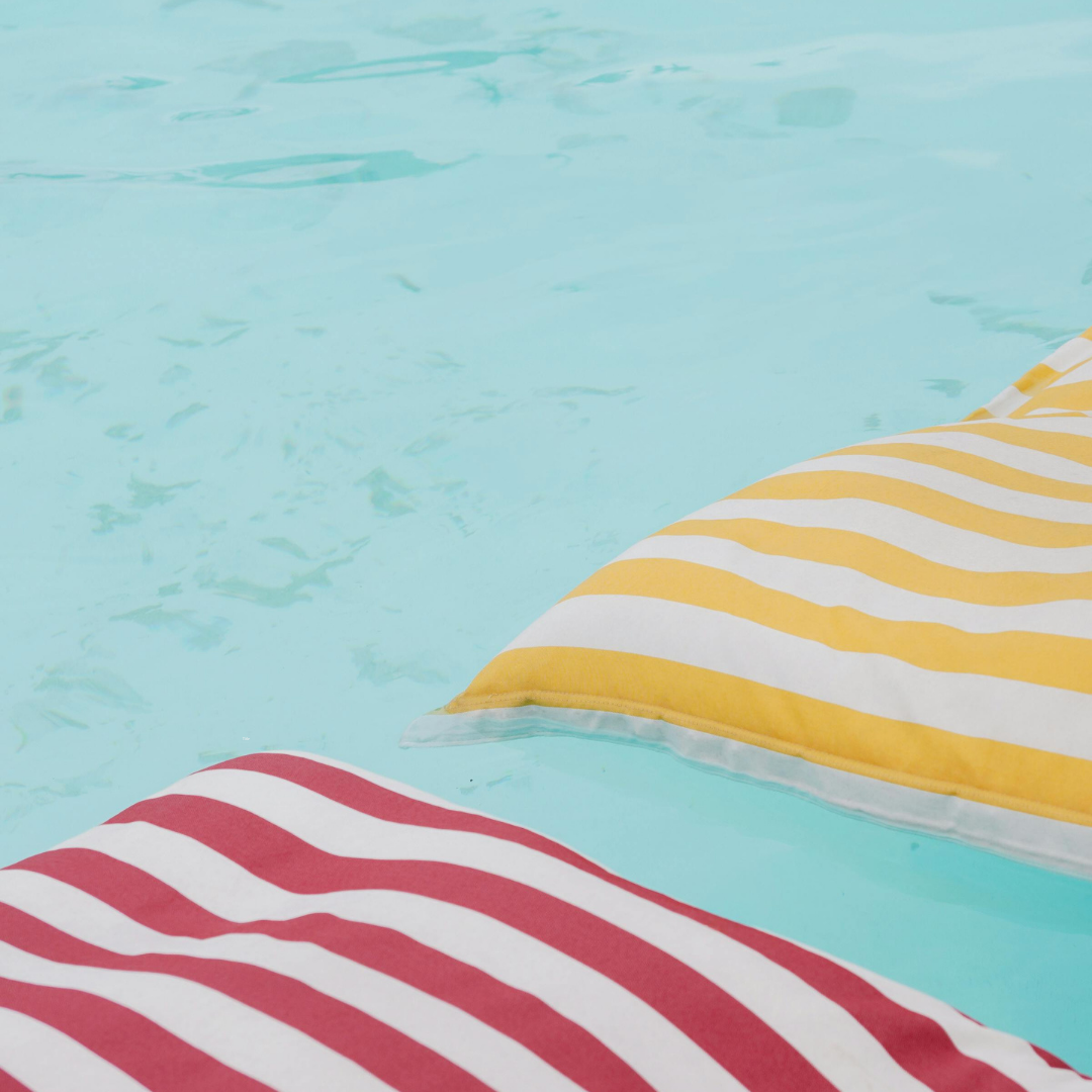 Close-up of striped yellow and white fabric and red and white fabric floating on a swimming pool with clear blue water.