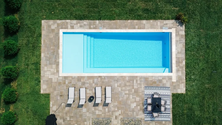 Aerial view of a rectangular pool with a light stone patio