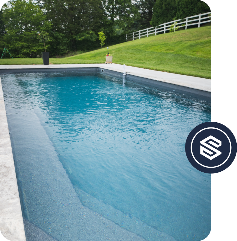 Empty backyard swimming pool with a grassy yard and trees in the background.