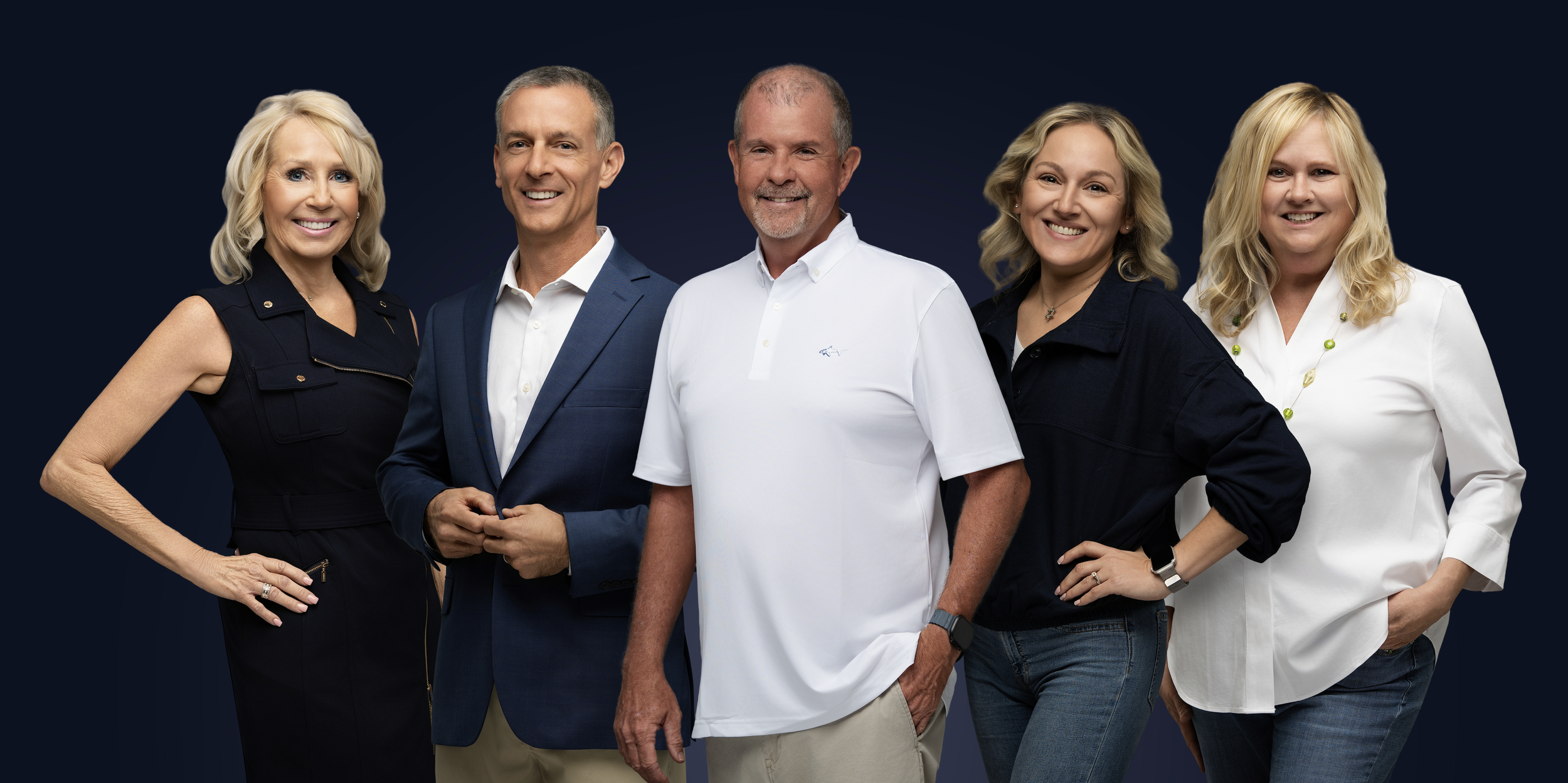 Group of five smiling adults standing against a dark background, dressed in business casual and casual attire.
